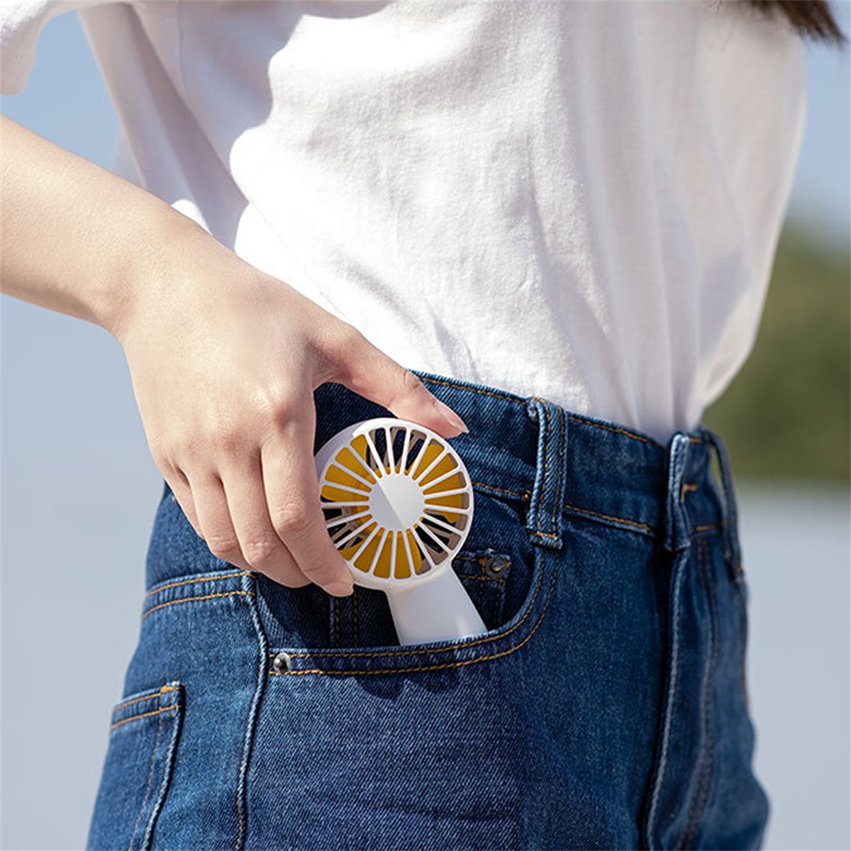 Die Hand einer Person, die einen kleinen weißen und gelben Ventilator in einer Jeans-Hosentasche hält.