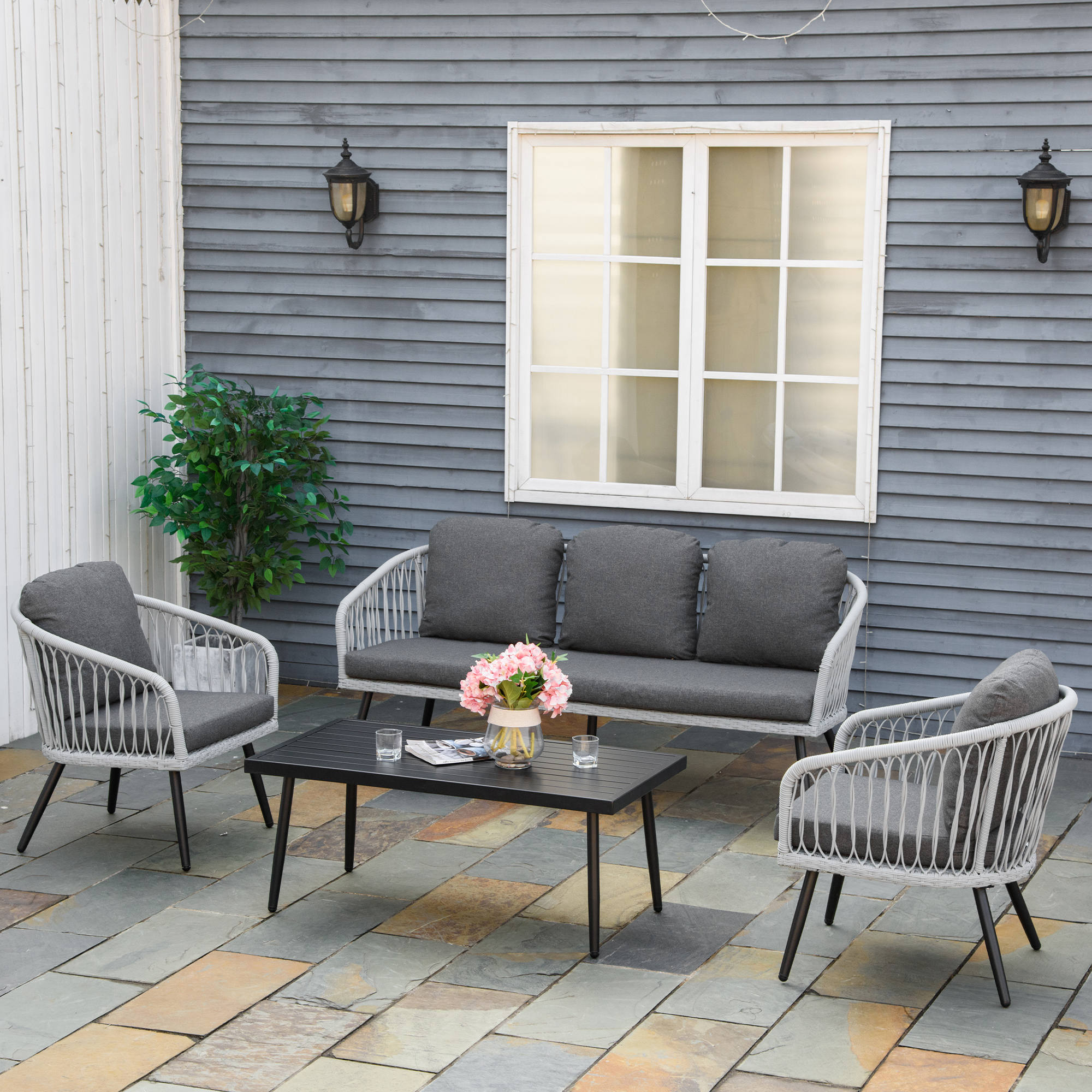 Terrassenset im Freien mit weißen Möbeln, grauen Kissen, schwarzem Tisch und grauer Wand.
