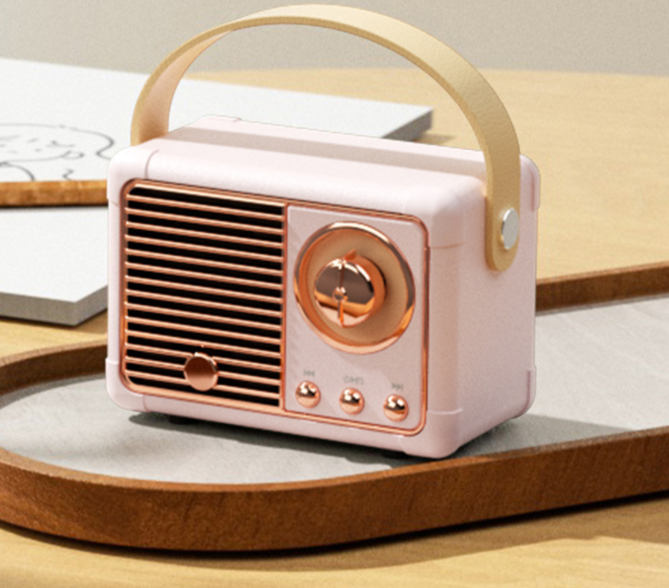 Ein kleiner, rosa Lautsprecher im Retro-Stil mit Griff, auf einem Holztablett. Verschwommener Hintergrund zeigt Holzoberfläche.