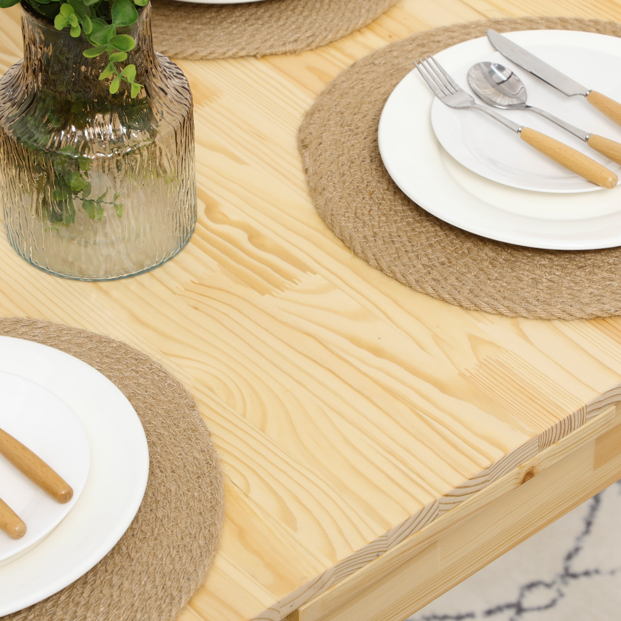 Holztisch mit Gedecken. Weiße Teller, Besteck und eine Vase mit Blumen sind sichtbar.