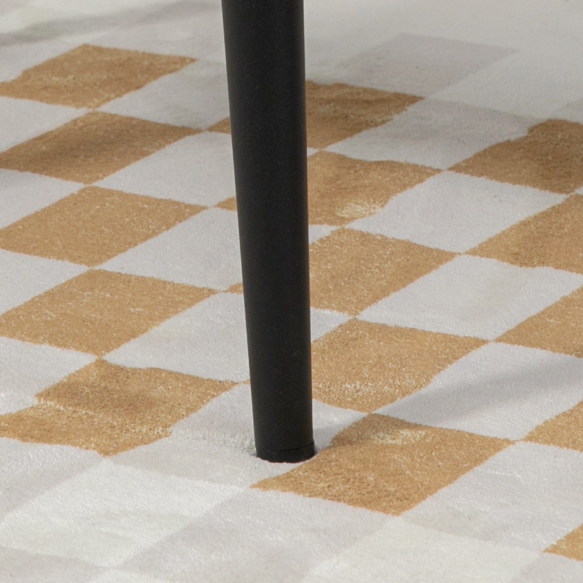 Schachbrettmuster-Teppich mit einem schwarzen Tischbein darauf. Die Quadrate sind beige und weiß.