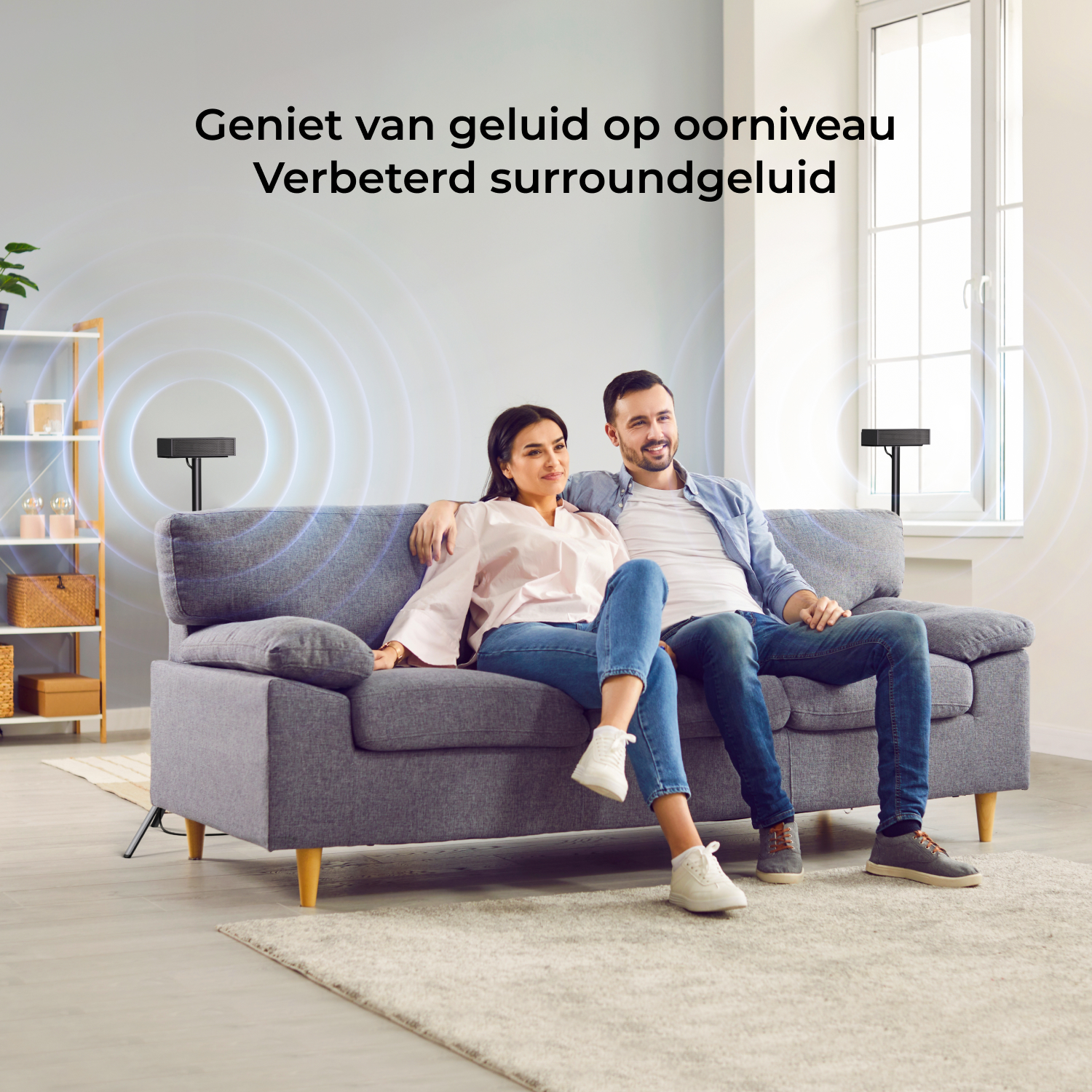Un couple assis sur un canapé gris, avec deux pieds d'enceintes produisant des ondes sonores.