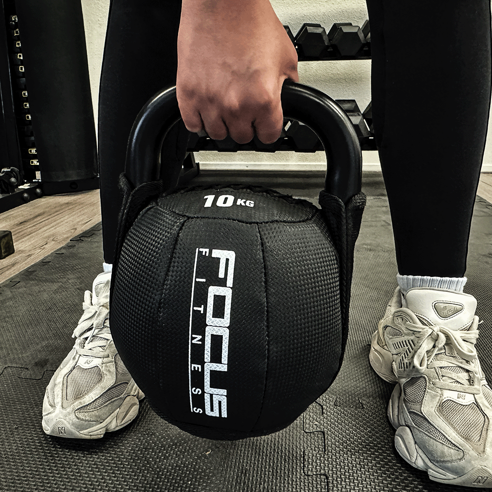 Person holding a black 10KG kettlebell. Focus Fitness logo is visible. Wearing black leggings and white shoes.