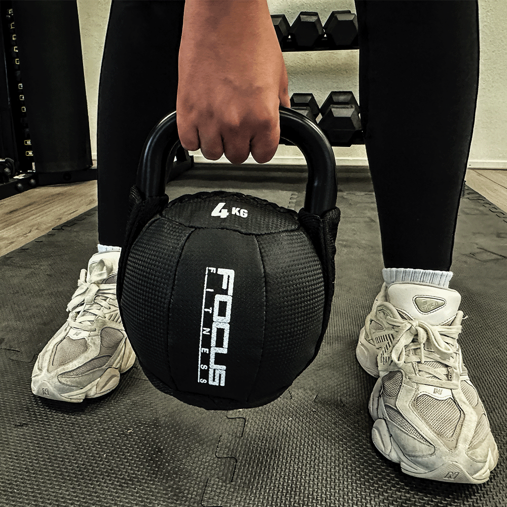 Person holding a black 4KG kettlebell. Focus Fitness logo is visible. Wearing black leggings and white shoes.