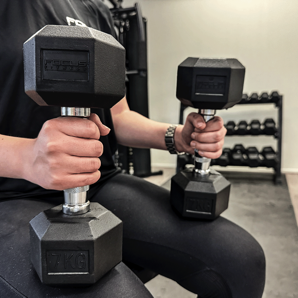 Personne tenant deux haltères noirs, un de 7 KG, dans une salle de sport.