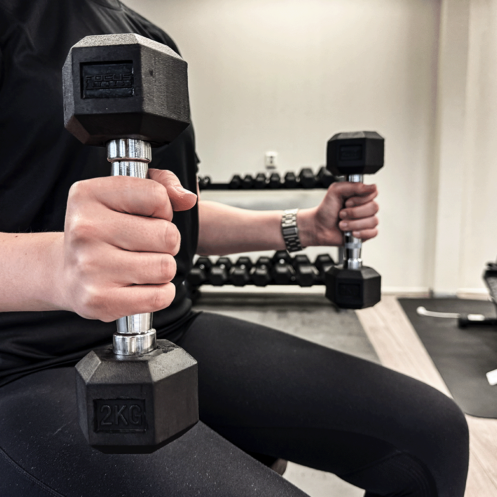 Person holding two black dumbbells, one 2 KG, in a gym.