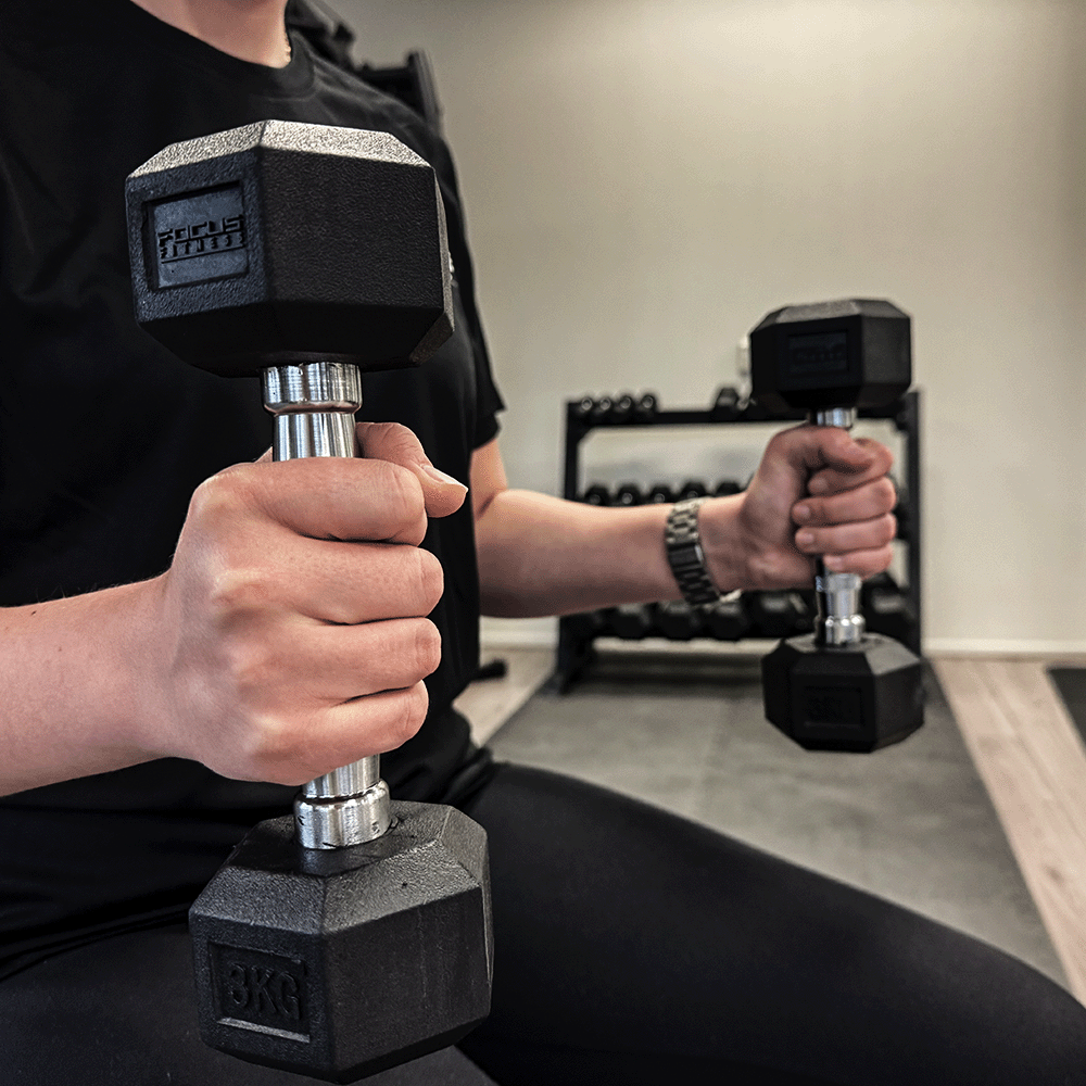 Two black dumbbells held by a person. They are in a gym setting.
