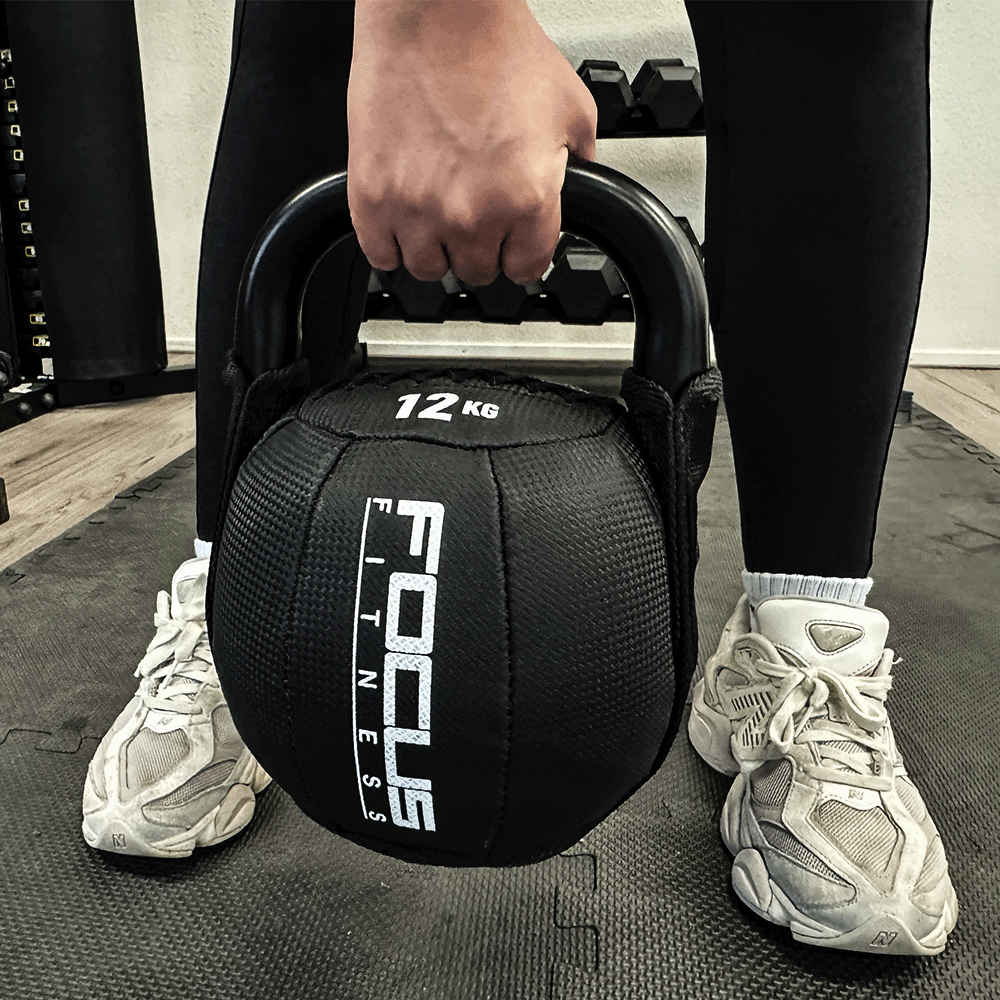 Person holding a 12 KG black kettlebell in a gym, wearing white sneakers.