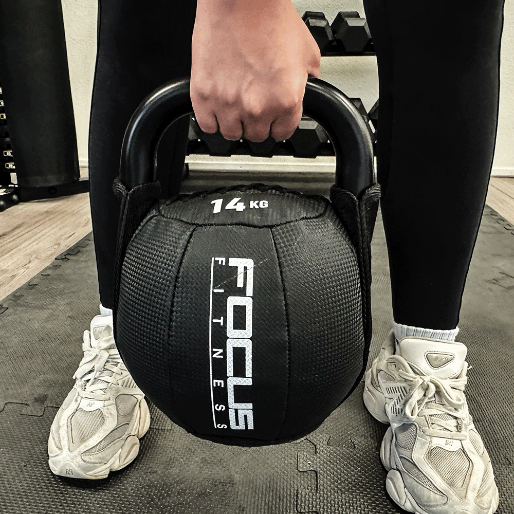 Person holding a black 14KG kettlebell. Focus Fitness logo is visible. Wearing black leggings and white shoes.