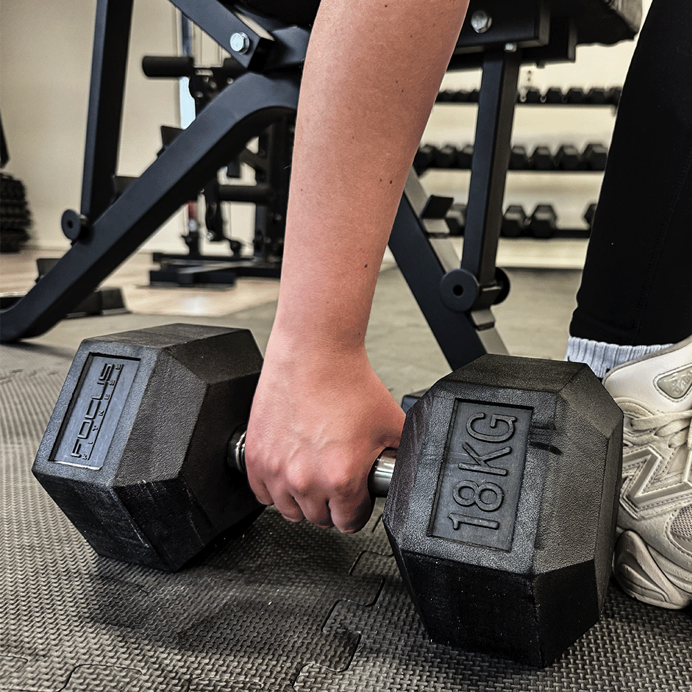 Person holding a 18 KG black dumbbell in a gym setting.