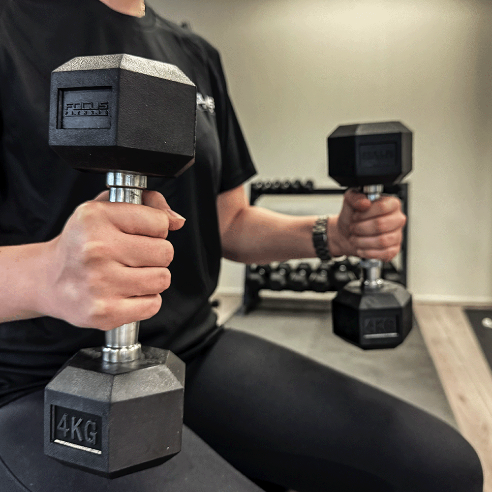 Person holding two black dumbbells, one 4 KG, in a gym.