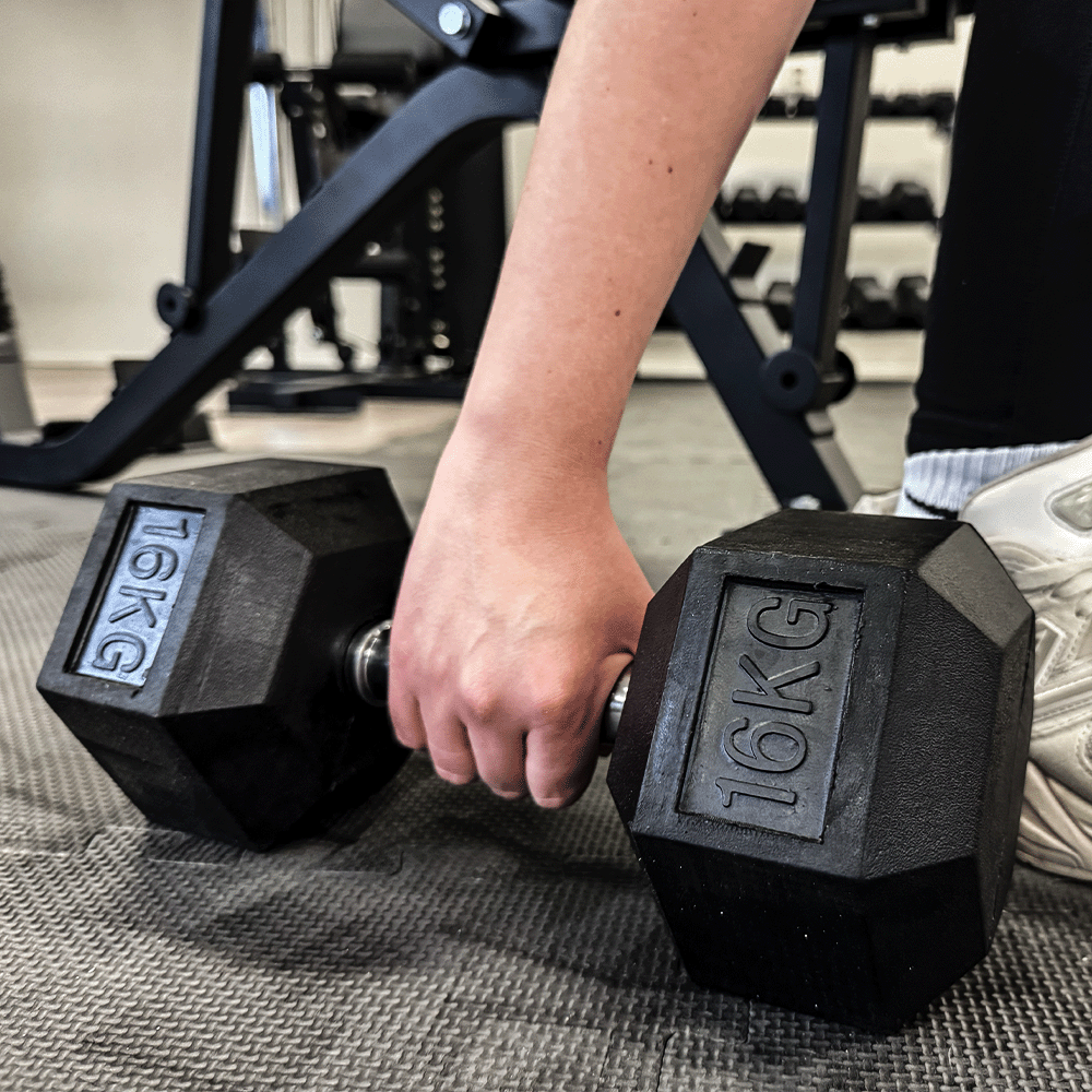 Persoon die een zwarte halter van 16KG vasthoudt in een sportschool.