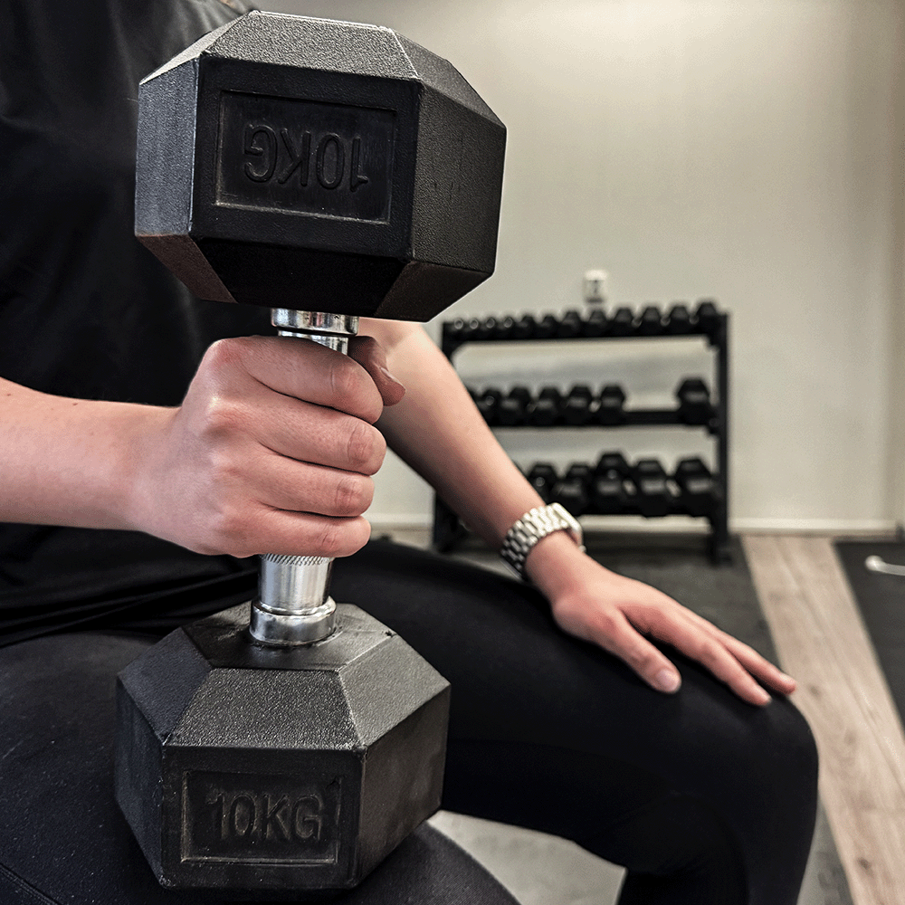 Person holding a 10 KG black dumbbell in a gym setting.