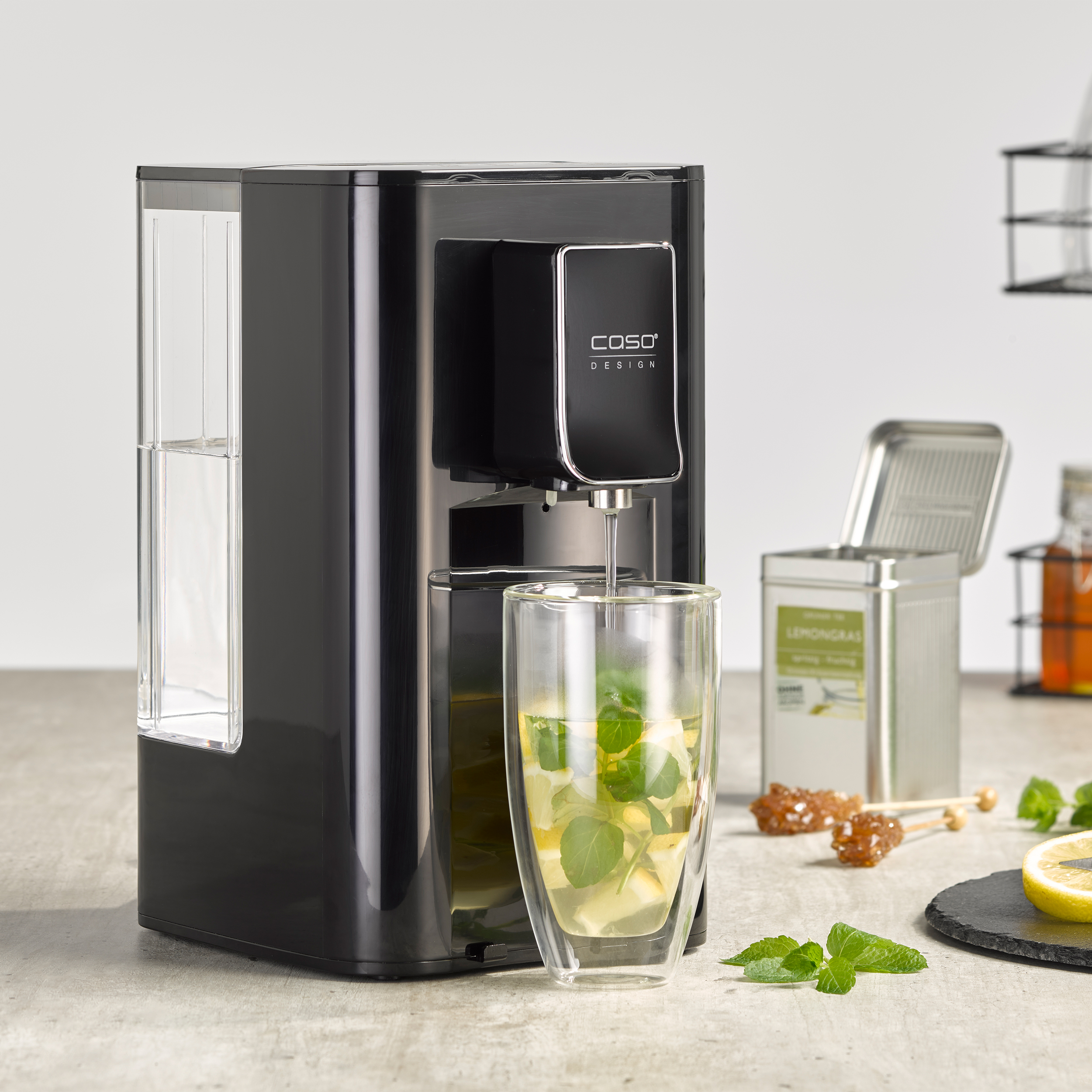 Ein schwarzer Wasserspender, der Wasser in ein Glas mit Tee und Extras abgibt.