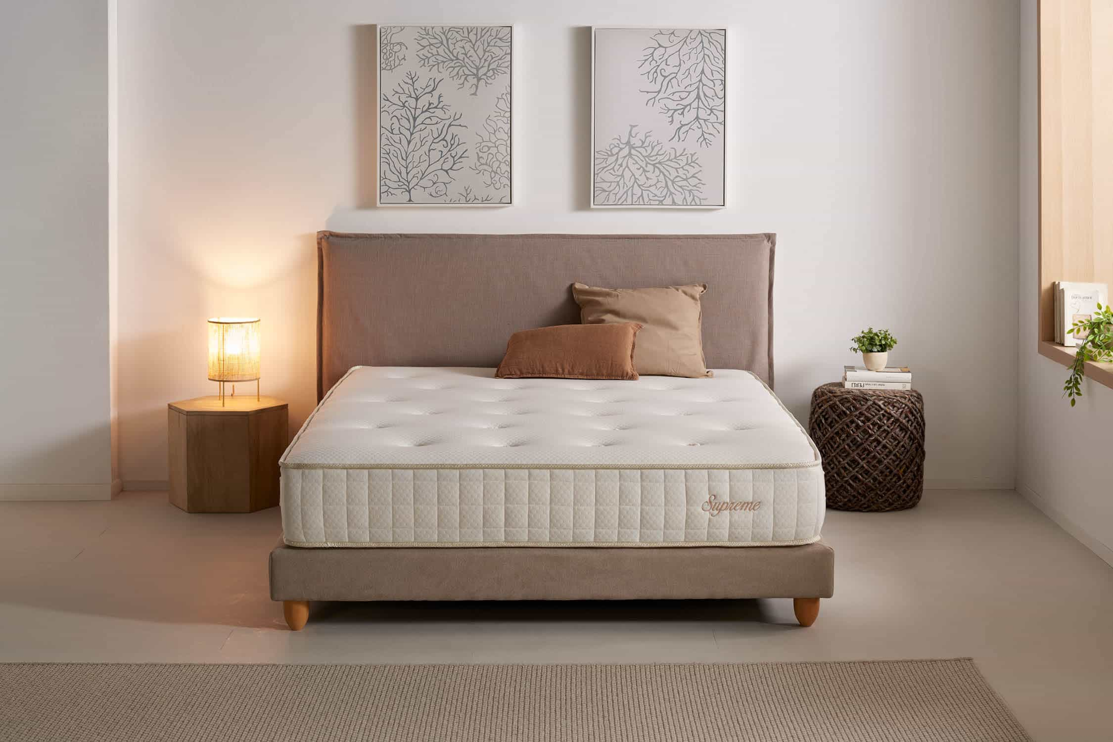 Colchón en una cama. Almohadas, lámpara y decoración. Marco de cama beige, colchón blanco con etiqueta Supreme.