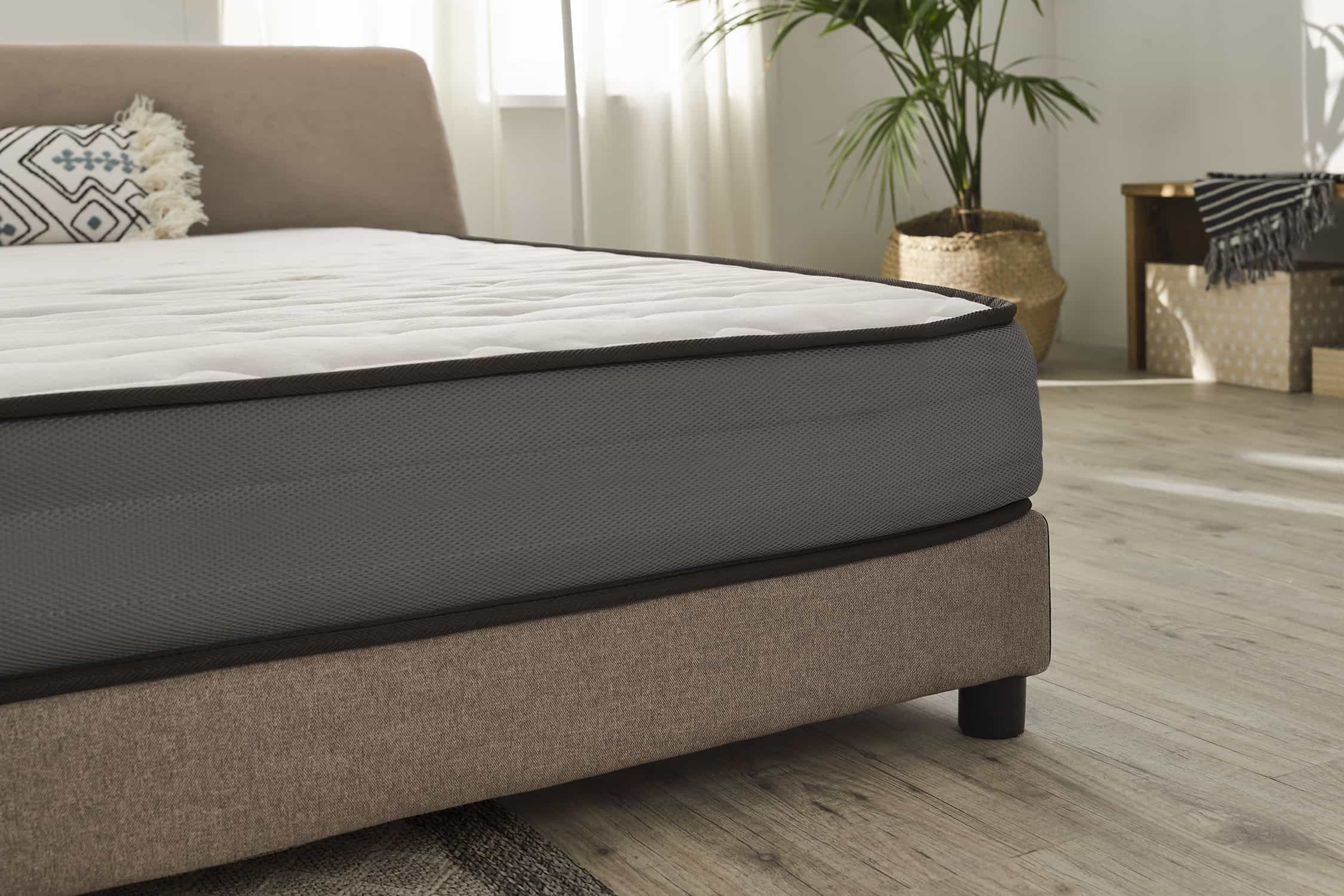 Primer plano de colchón en un marco de cama. Colchón blanco con borde gris. Marco de cama beige.