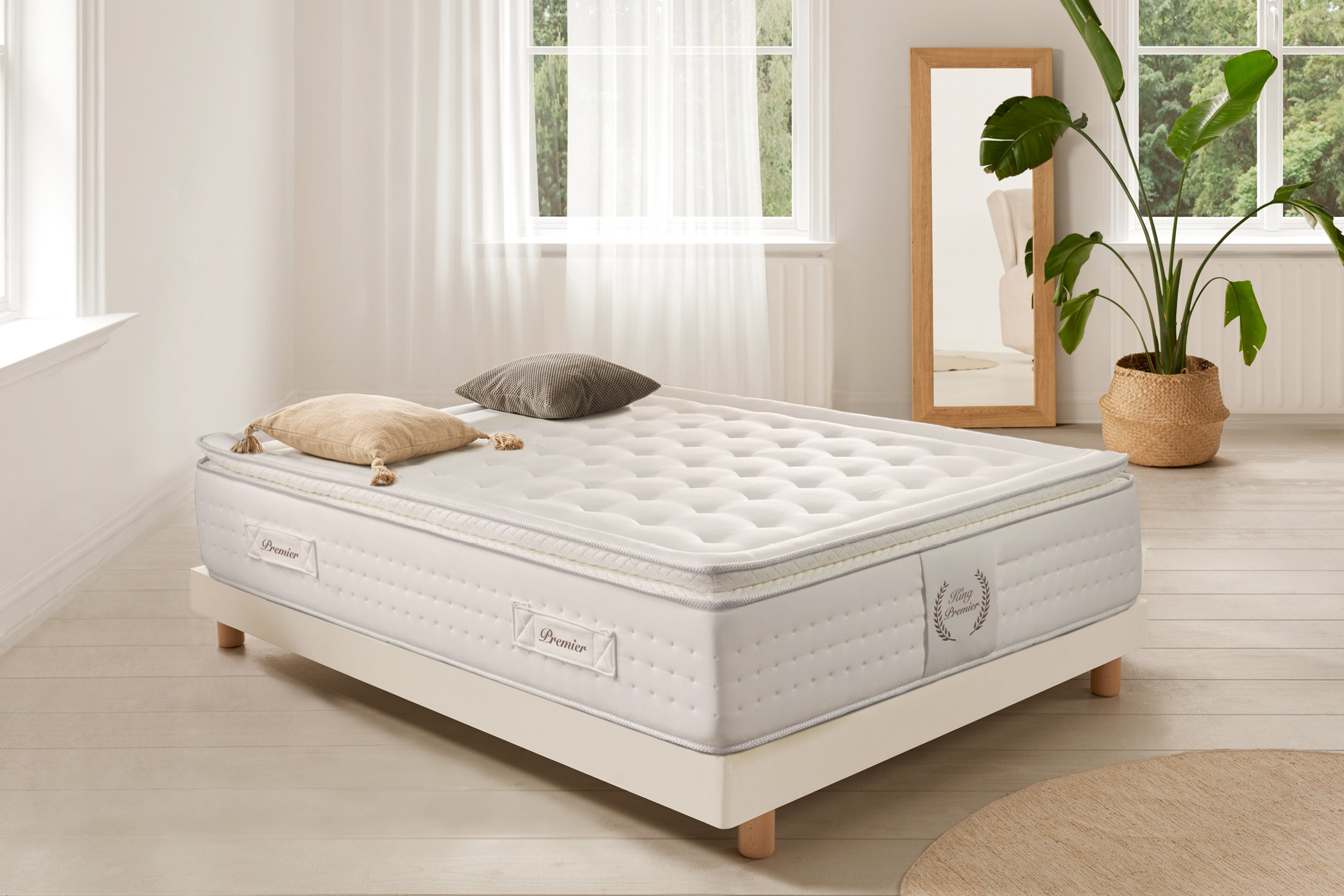 Escena de dormitorio con colchón en cama, almohadas. Espejo al fondo, plantas. Colores neutros.