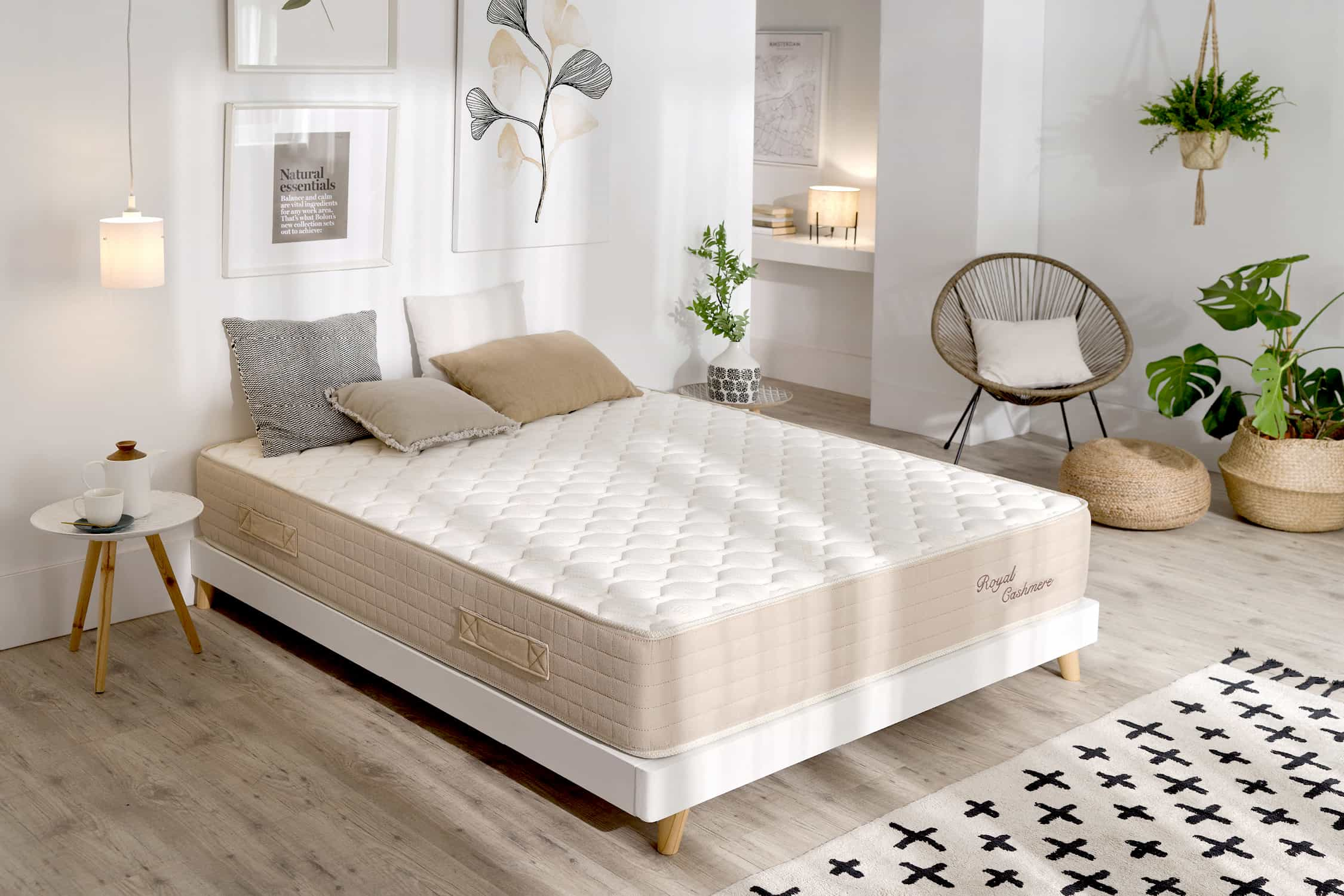 Dormitorio con colch ón sobre somier blanco, almohadas, plantas y decoración. Suelo de madera, paredes blancas.