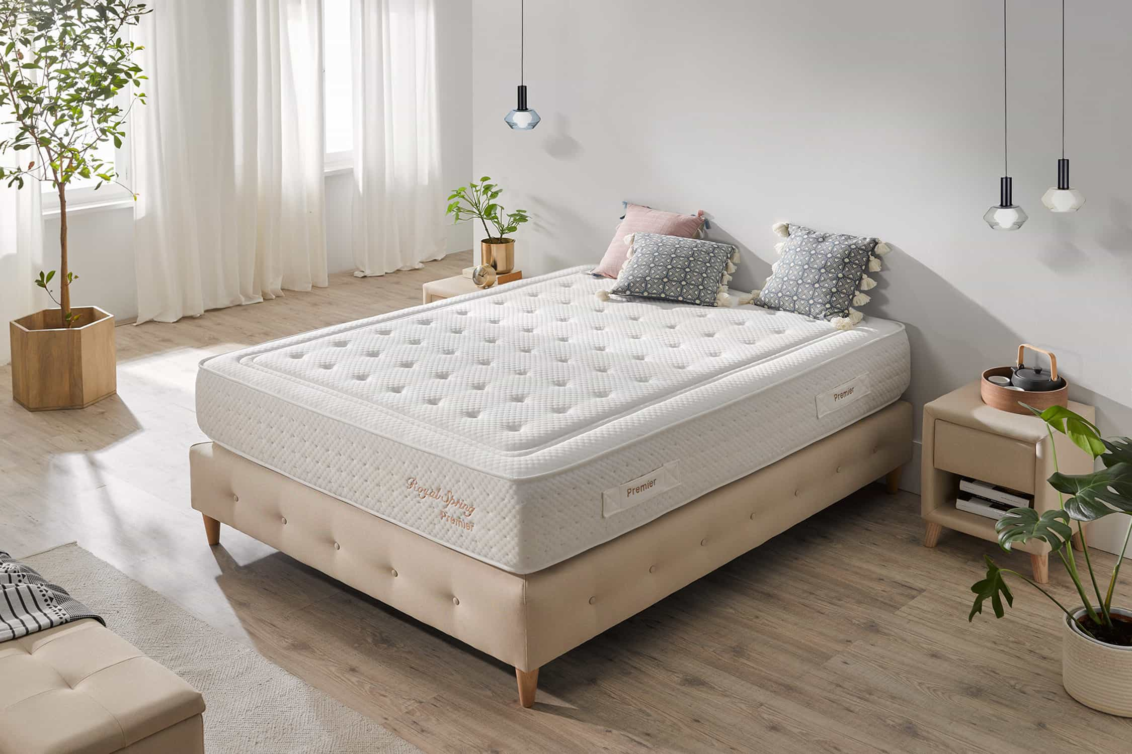 Dormitorio con colchón en cama, almohadas, plantas y mesita de noche con lámpara. Colores neutros.