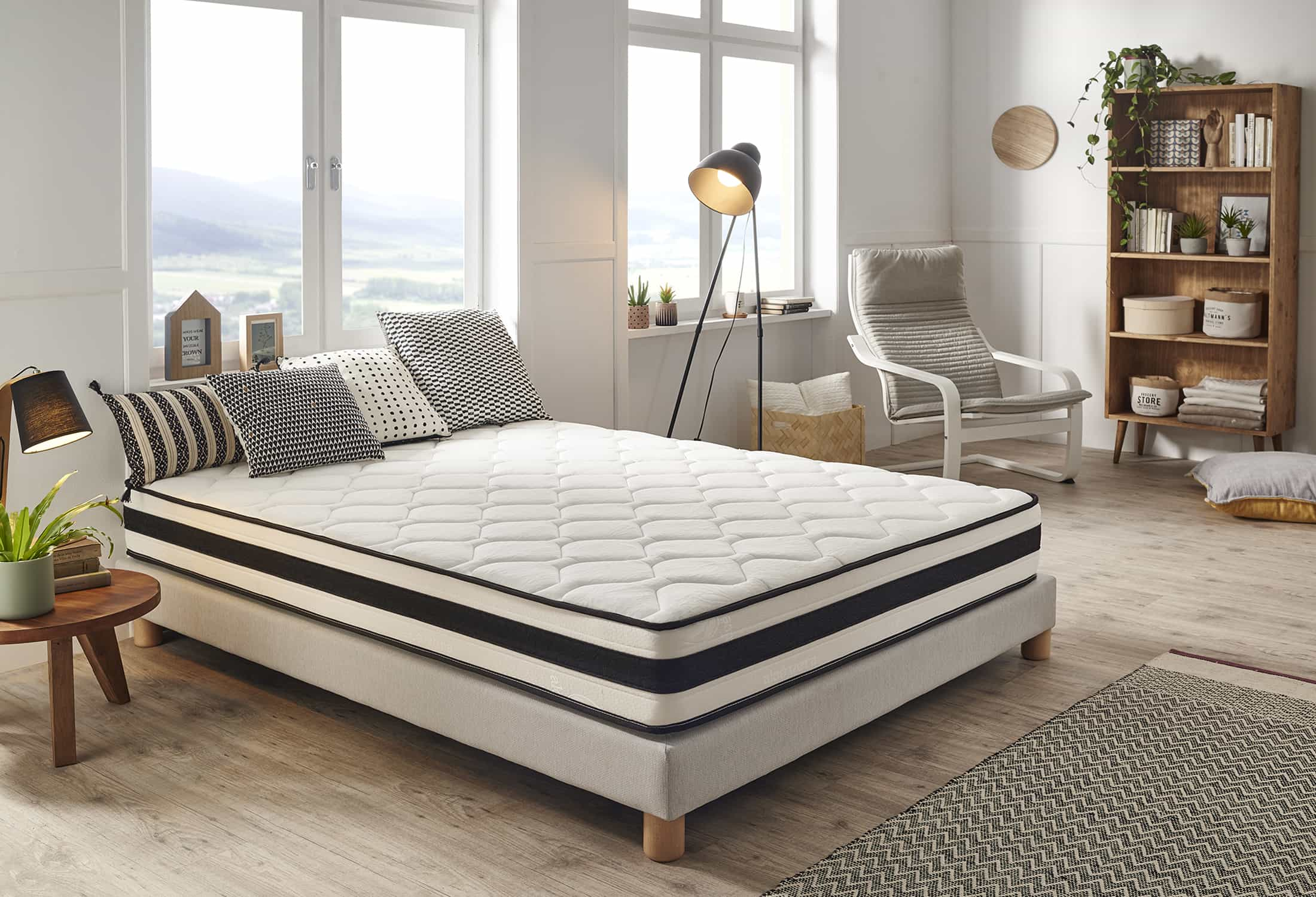 Colchón blanco con almohadas. Acentos a rayas blancas y negras. Ventanas y silla al fondo.