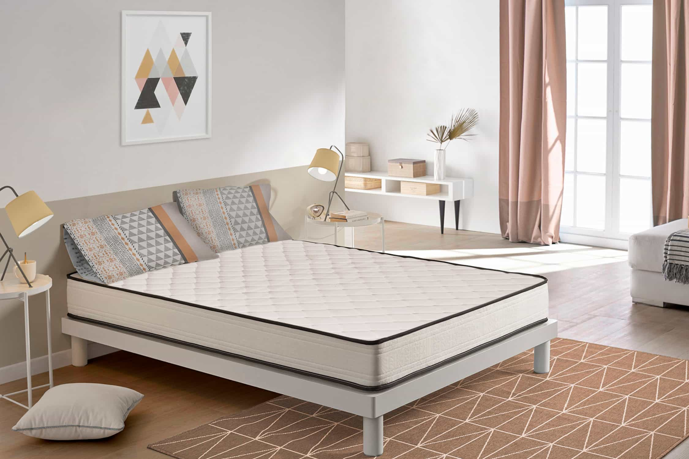 Colchón blanco en estructura de cama, almohadas y arte mural geométrico. Cortinas rosas.