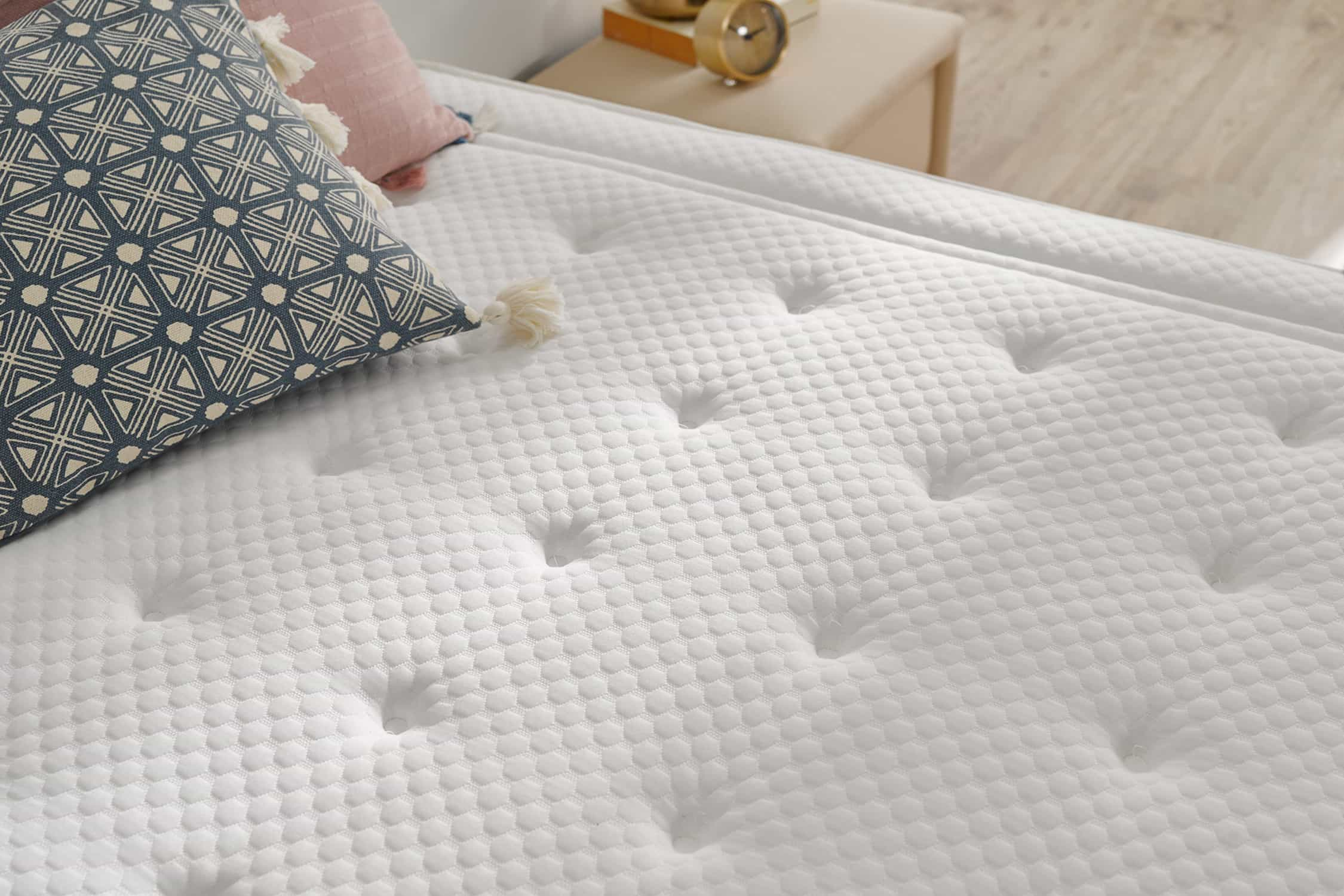 Primer plano de un colchón blanco con botones y un patrón de diamantes. Una almohada a la izquierda.
