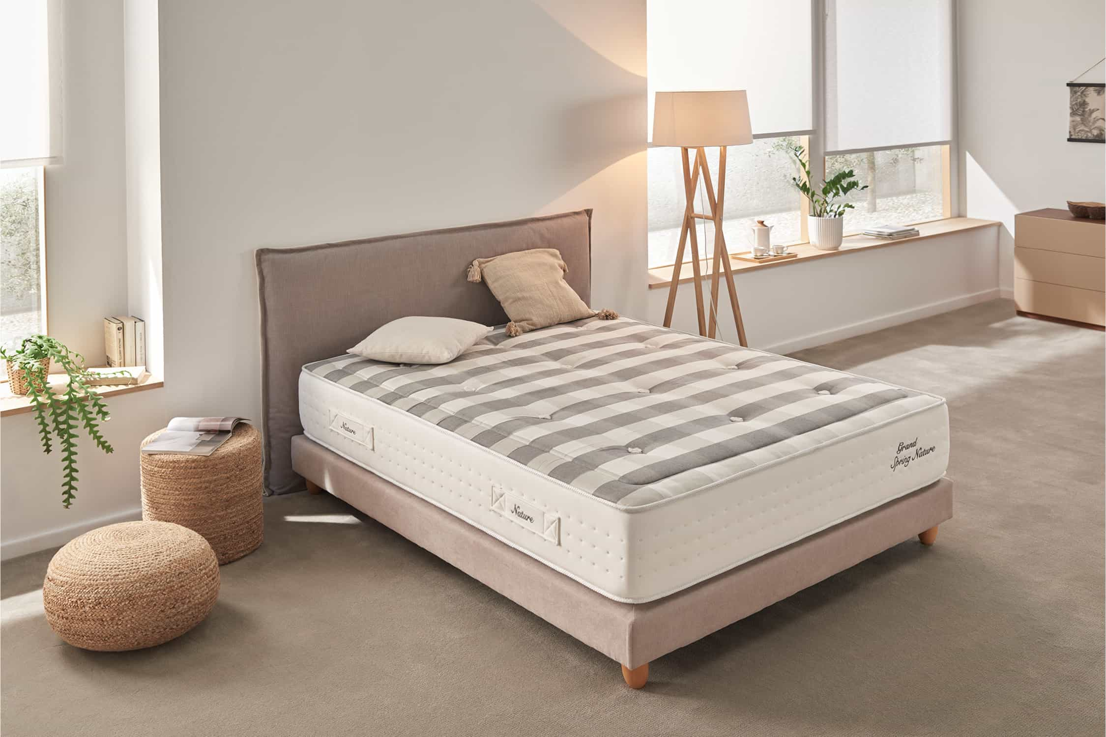 Cama con colchón a rayas grises y blancas en una habitación. Incluye almohadas, lámpara y un taburete.