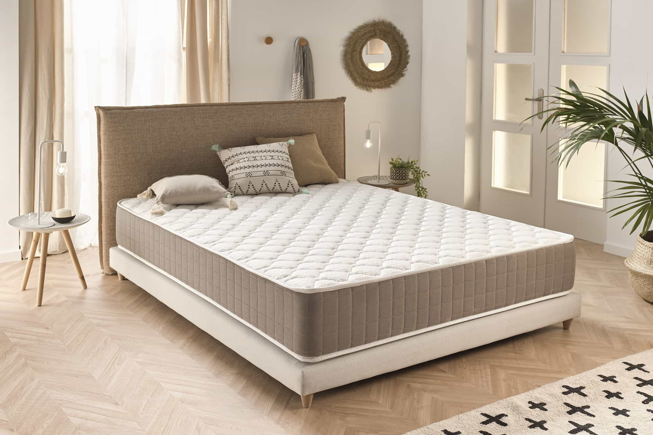 Una cama con colchón acolchado blanco en un dormitorio. Incluye almohadas, una alfombra y una planta.