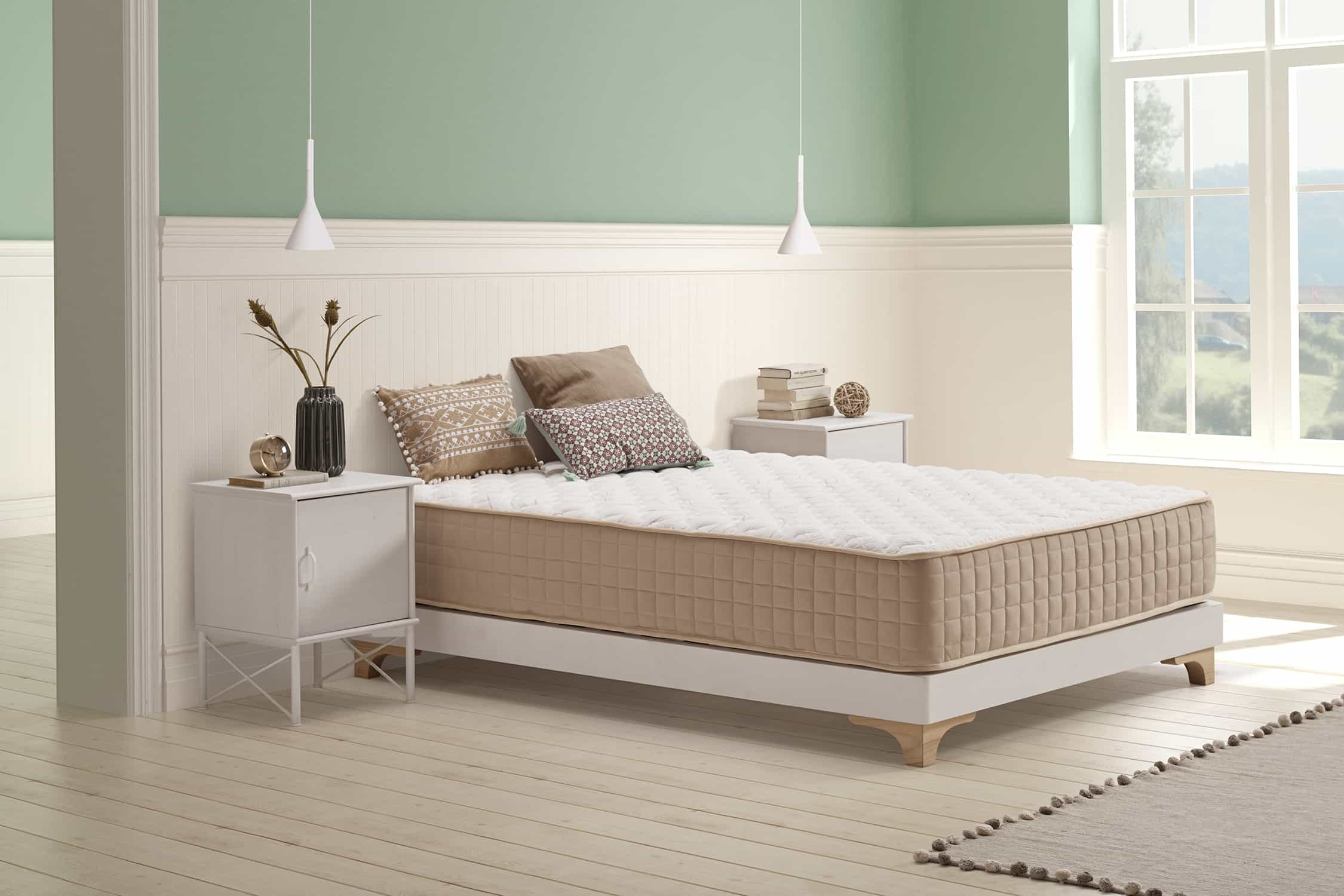 Cama con colchón beige, marco blanco, almohadas, mesitas de noche y pared.