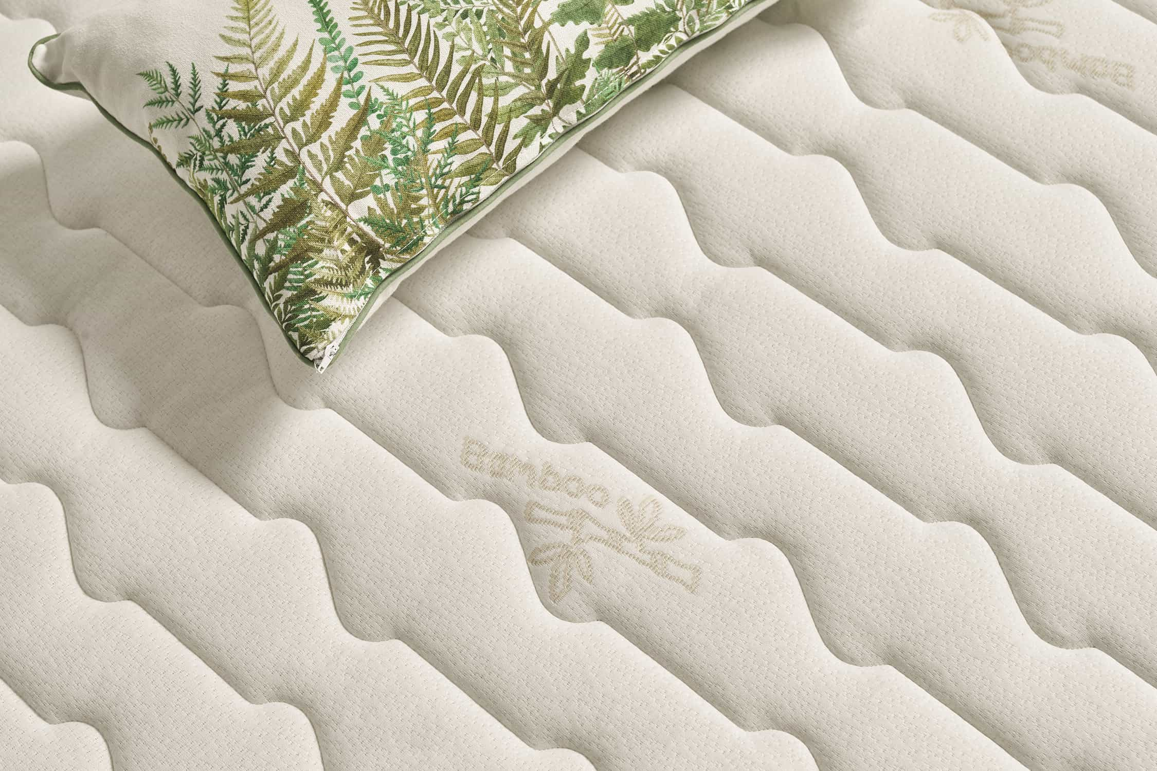 Primer plano de una almohada sobre un colchón blanco con un patrón de hojas verdes.