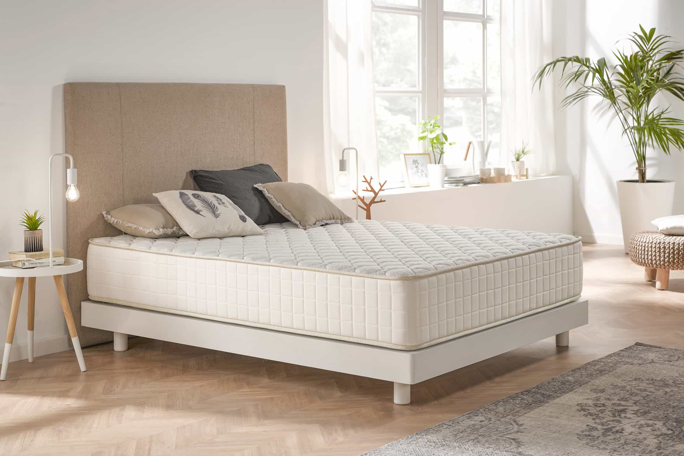 Un dormitorio con cama blanca, almohadas, alfombra y ventana con luz natural.
