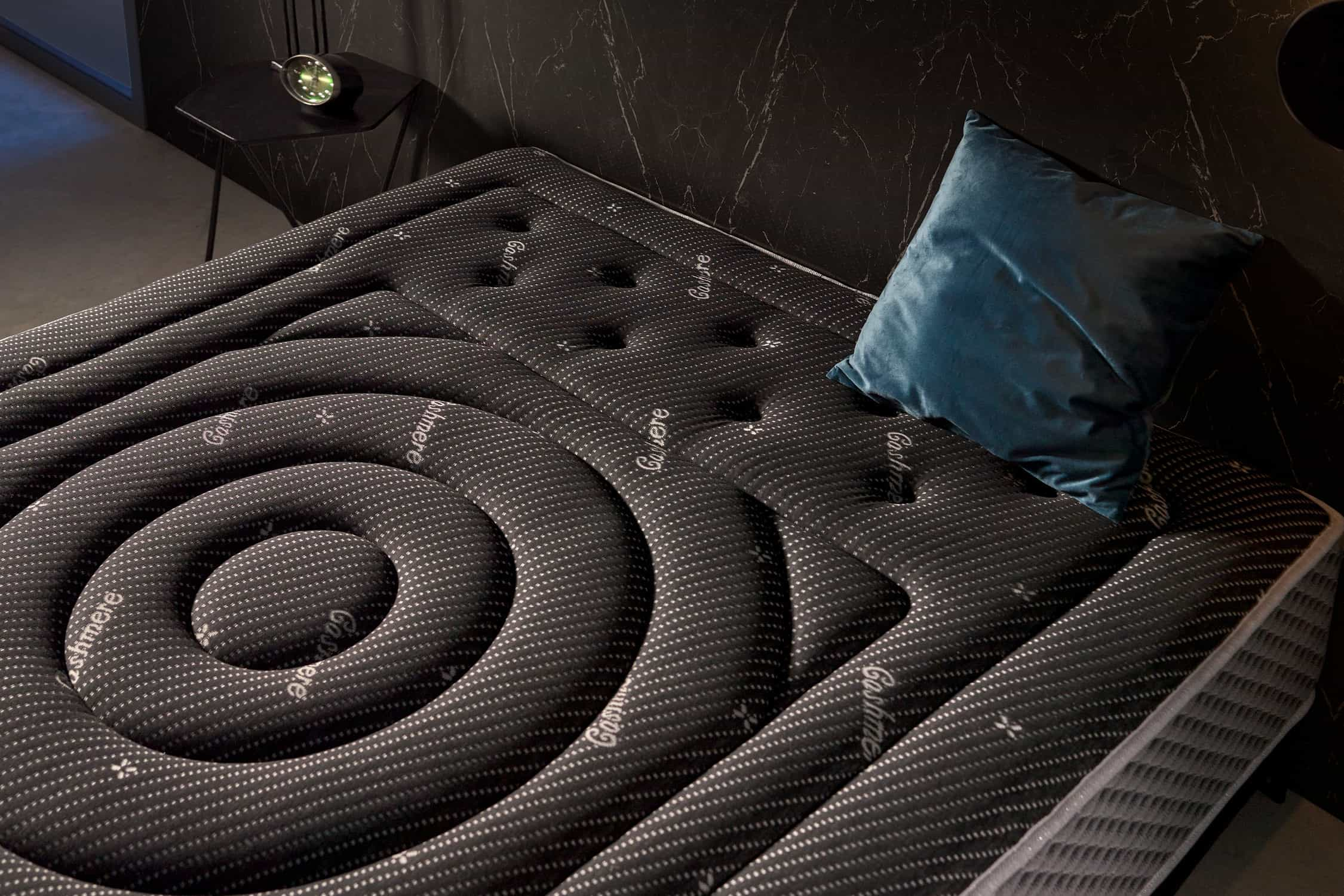 Colchón estampado gris y negro con almohada azul sobre fondo oscuro.