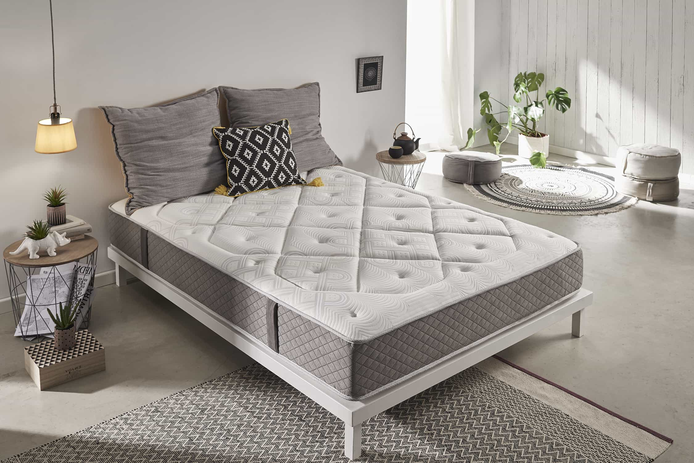 Dormitorio con cama, almohadas, lámparas, plantas y alfombra. La cama tiene marco blanco.