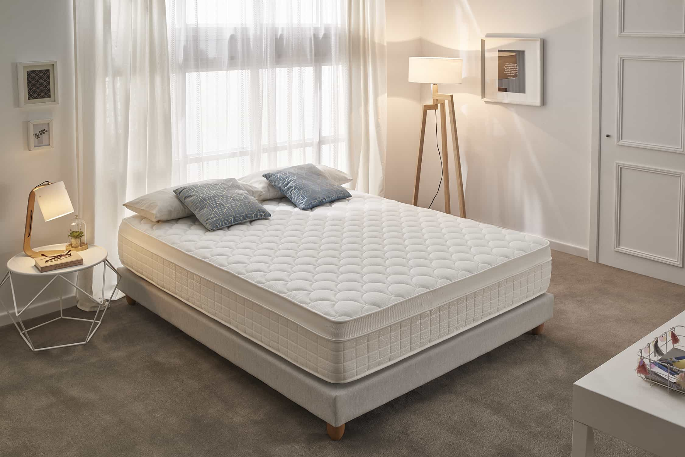 Cama con colchón, almohadas, lámparas, ventana y decoración.