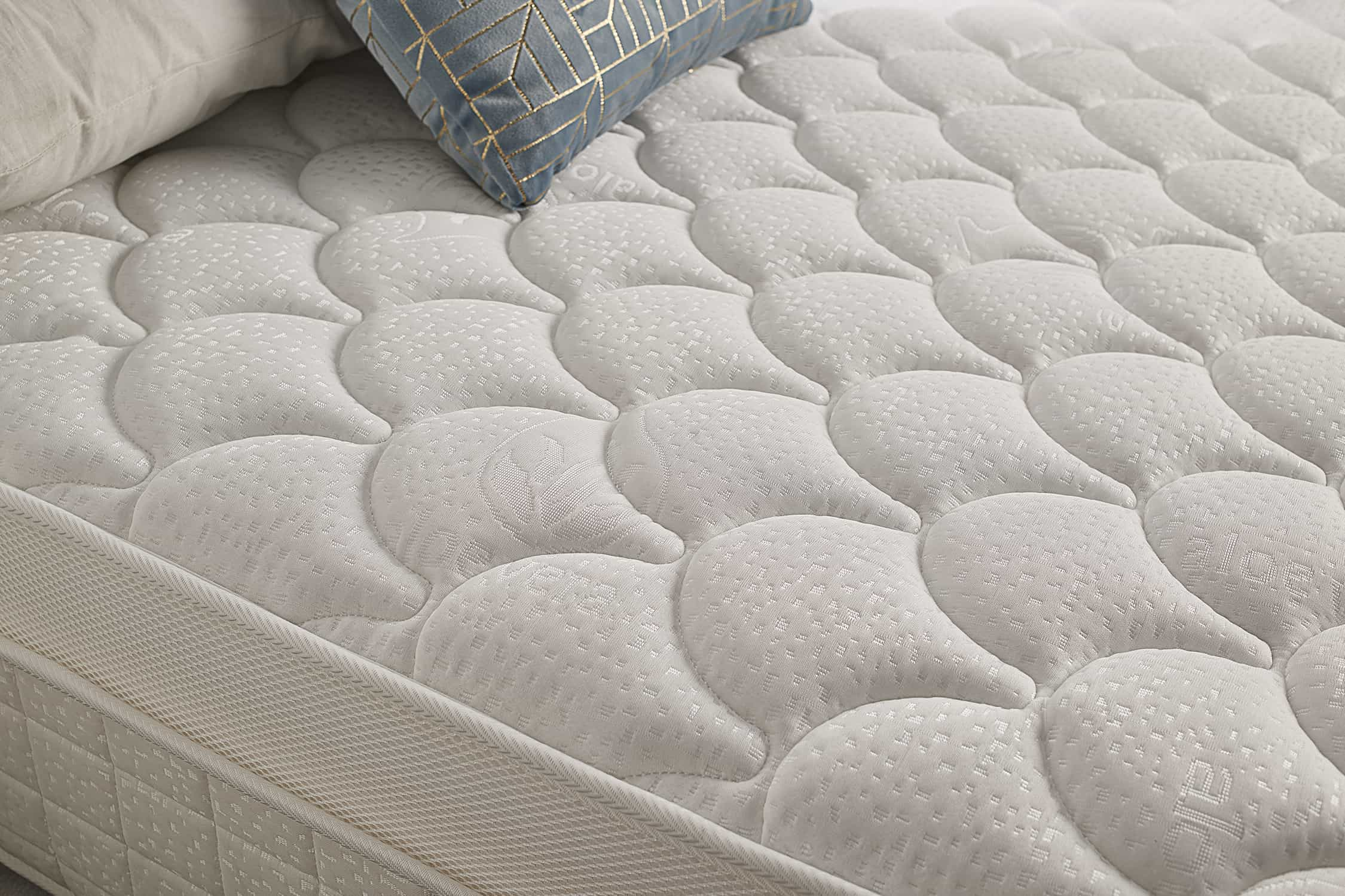 Primer plano de un colchón blanco con diseño acolchado. Tiene una almohada dorada y azul encima.