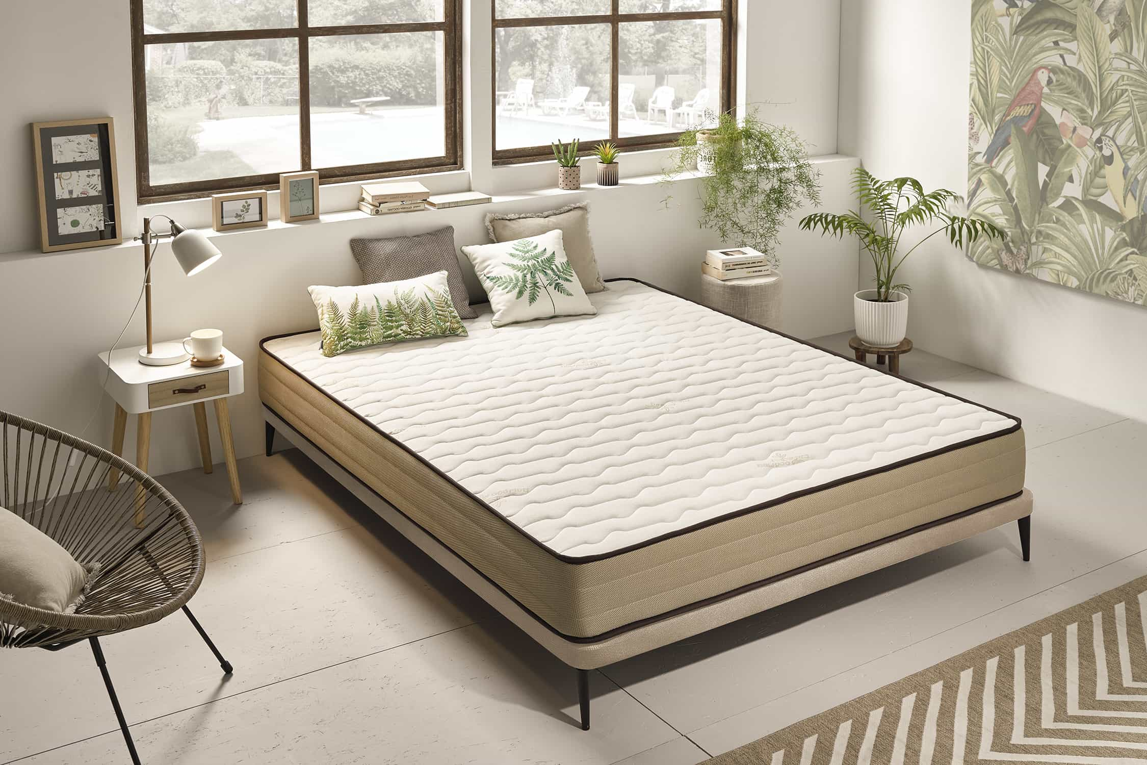 Dormitorio con cama, almohadas y plantas. La cama tiene un marco beige.