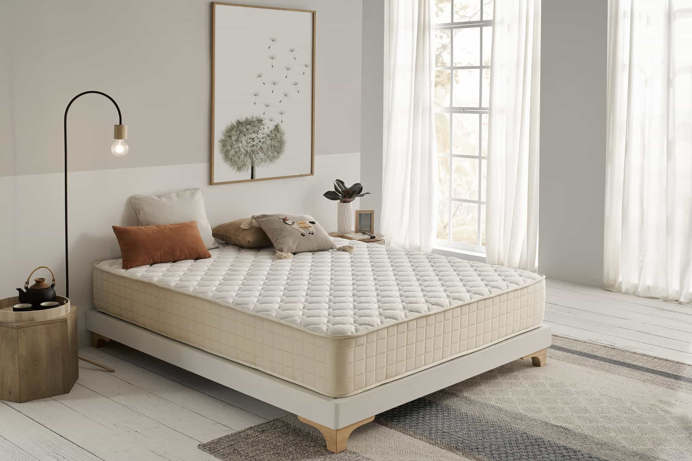Escena de dormitorio con cama, colchón, cuadro, lámpara, alfombra y cojines.