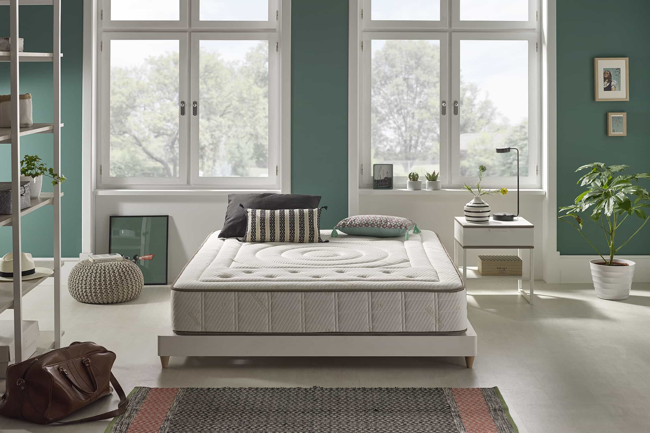 Escena de dormitorio con cama, colchón, almohadas y ventanas.