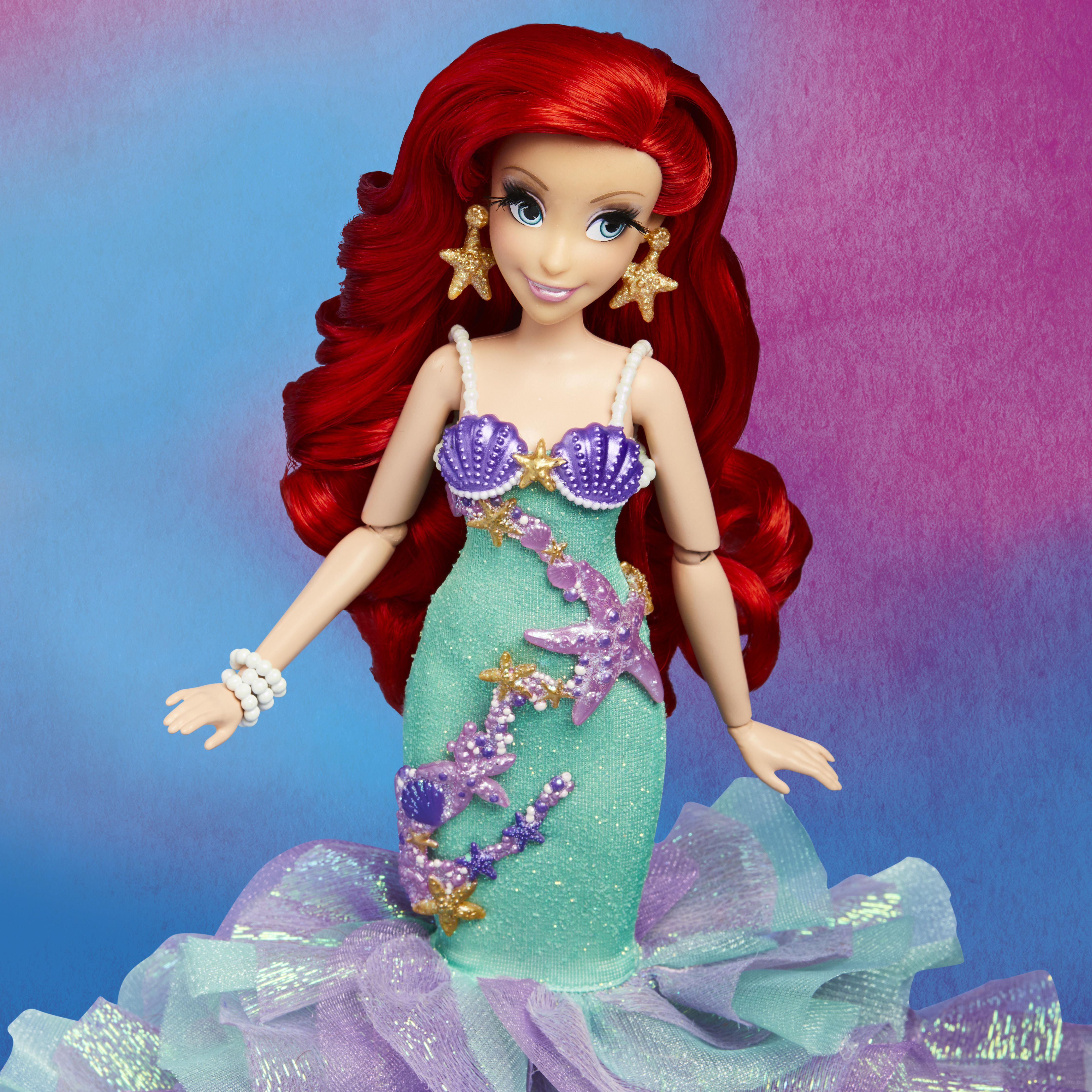 Eine Ariel-Puppe mit roten Haaren, einem türkisfarbenen Kleid und goldenen Accessoires, mit buntem Hintergrund.