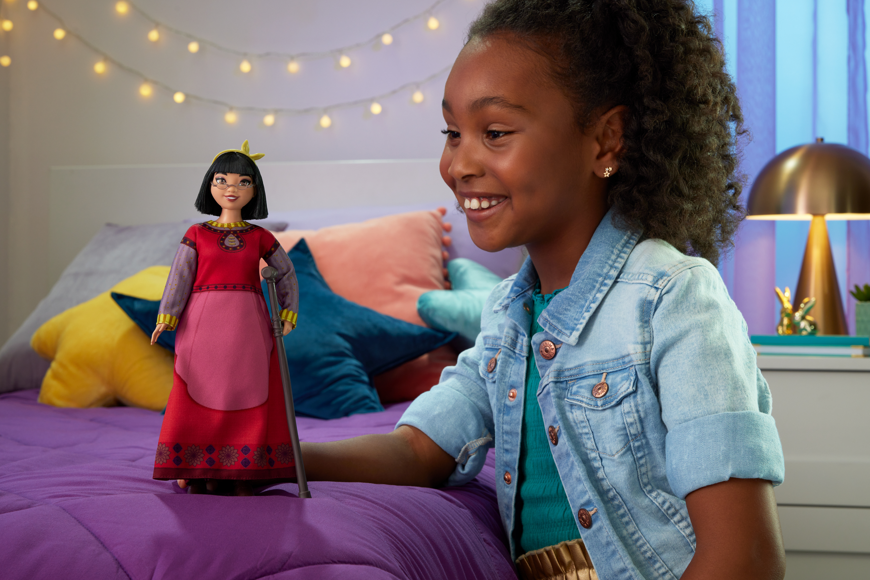 Dziewczyna uśmiecha się do lalki. Lalka przedstawia starszą kobietę z laską.