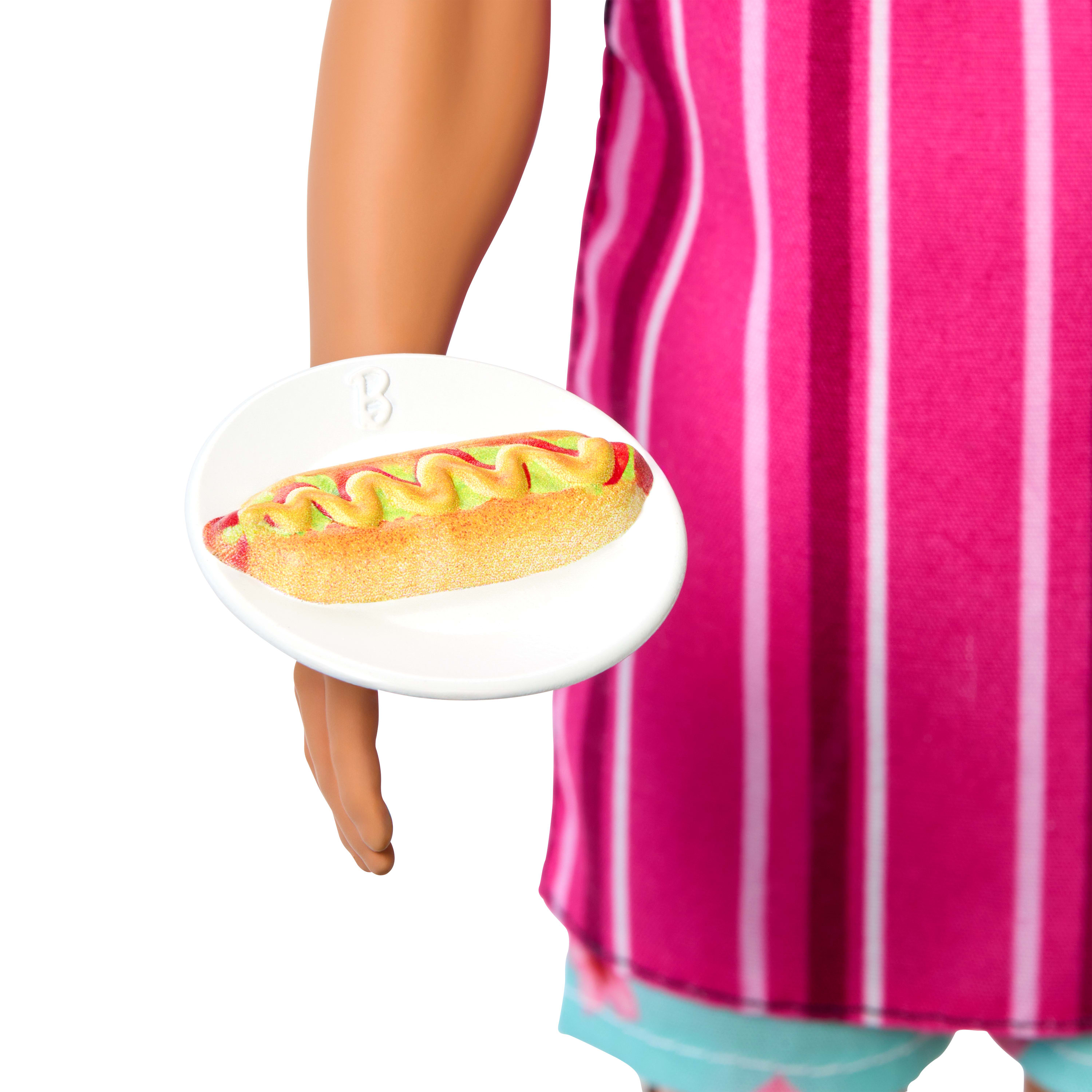 Die Hand einer Puppe, die einen Teller mit einem Hotdog mit Senf und Relish hält.