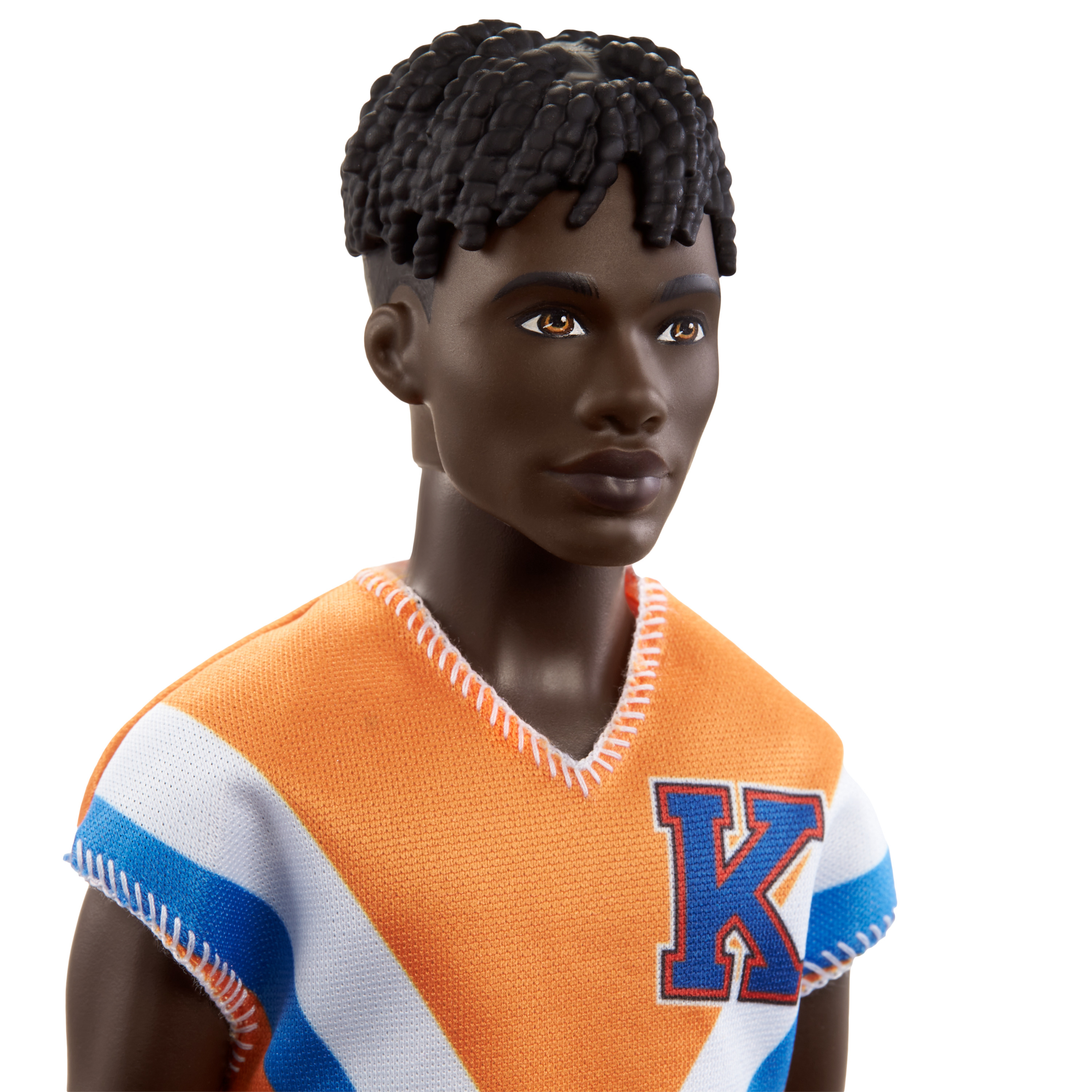 Eine schwarze männliche Puppe mit kurzem Afro, trägt ein orange-blaues Hemd mit einem 'K'.