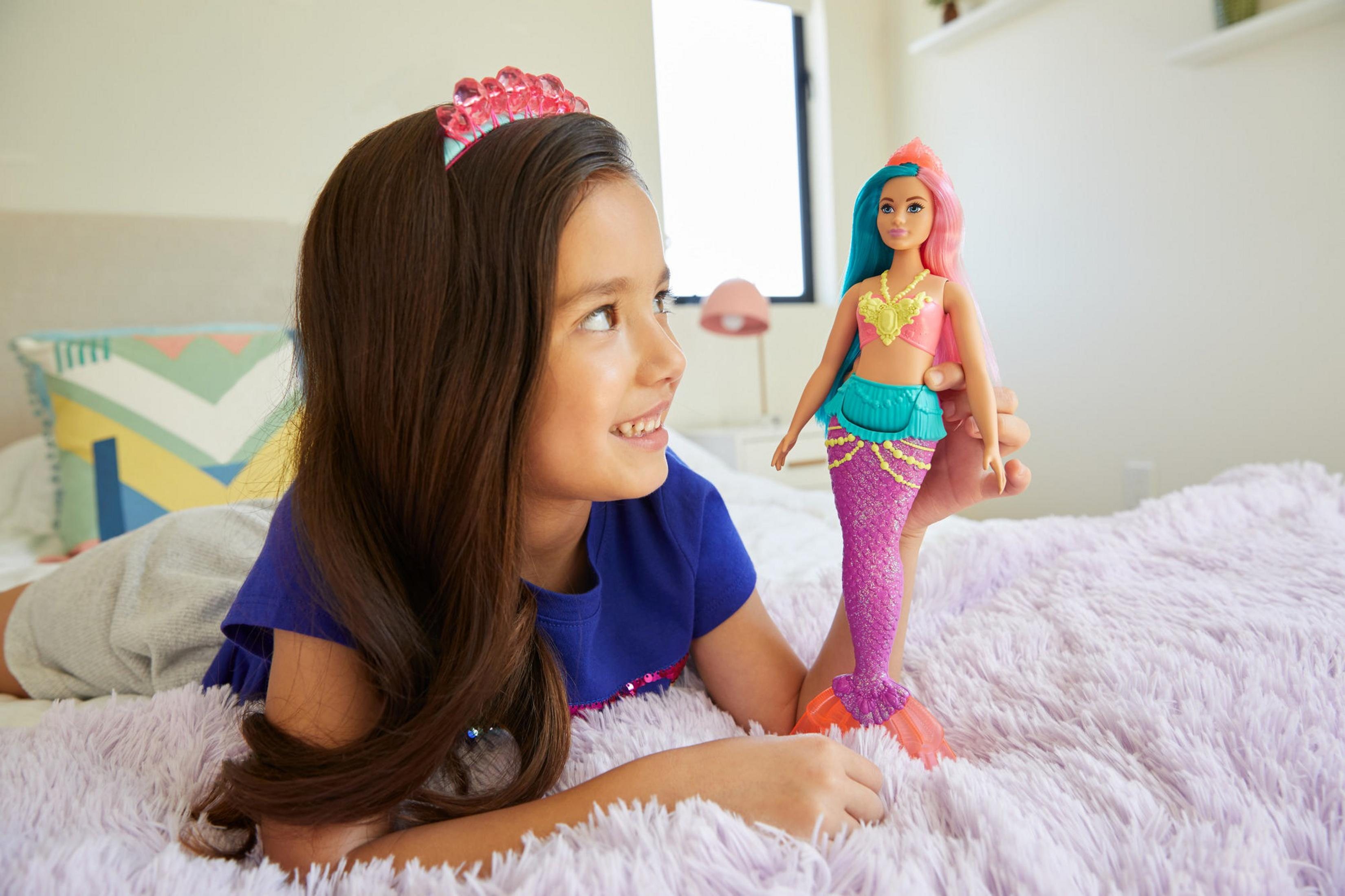 Une fille regardant une poupée sirène Barbie, allongée sur un lit.