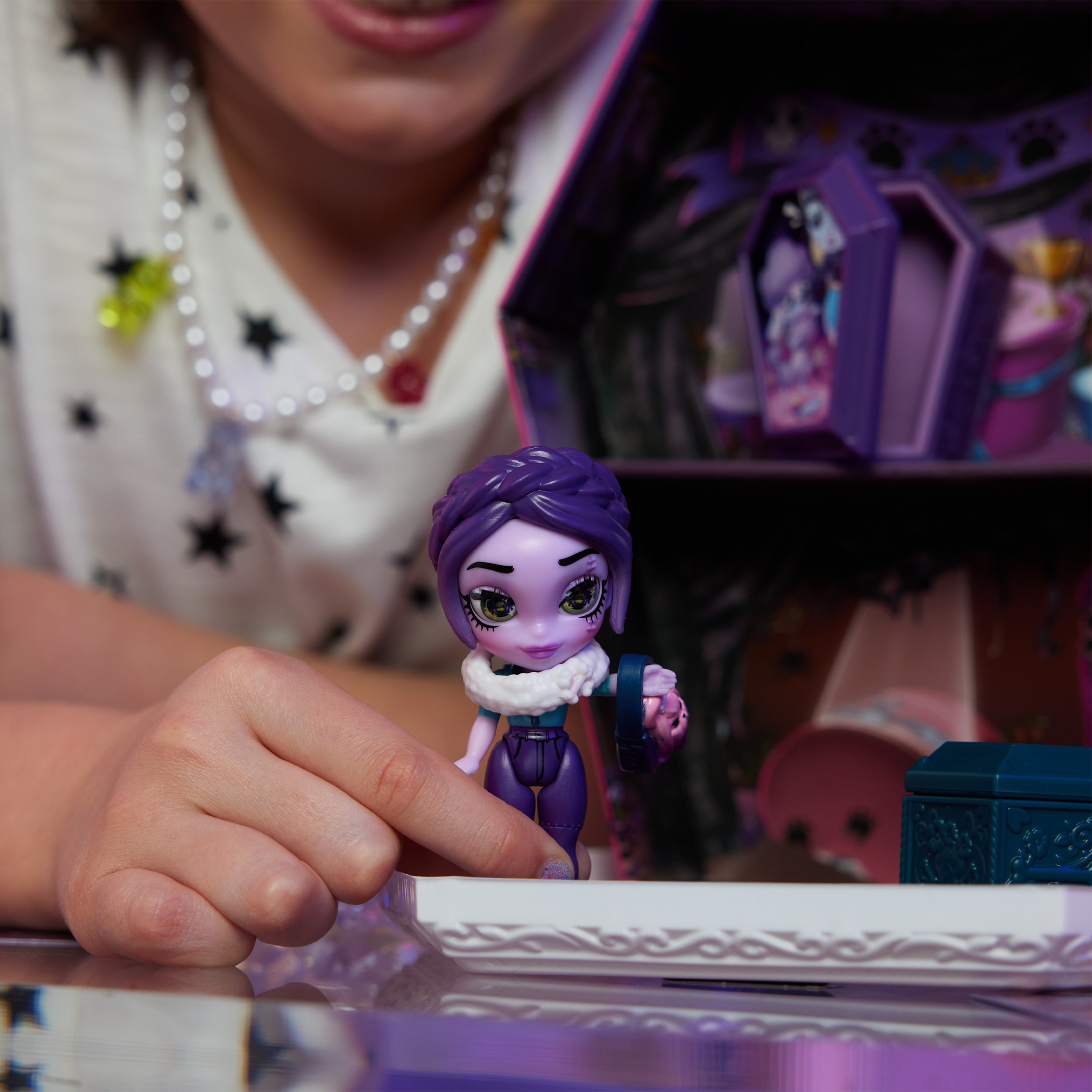 La mano de una niña sosteniendo una muñeca. La muñeca tiene cabello morado y está frente a un juego morado.