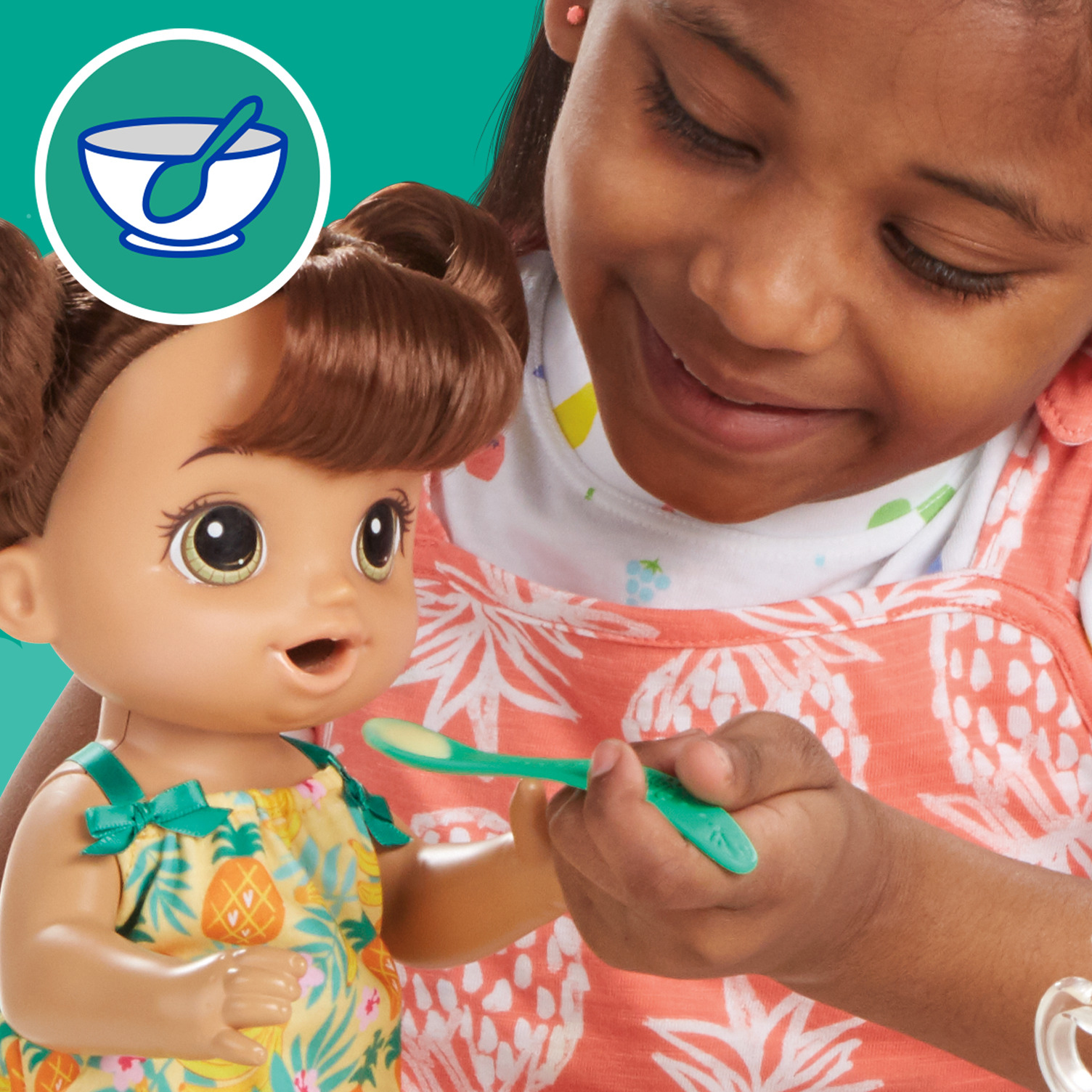 Ein Mädchen füttert eine Baby Alive Puppe mit einem grünen Löffel. Die Puppe trägt ein Blumenkleid.