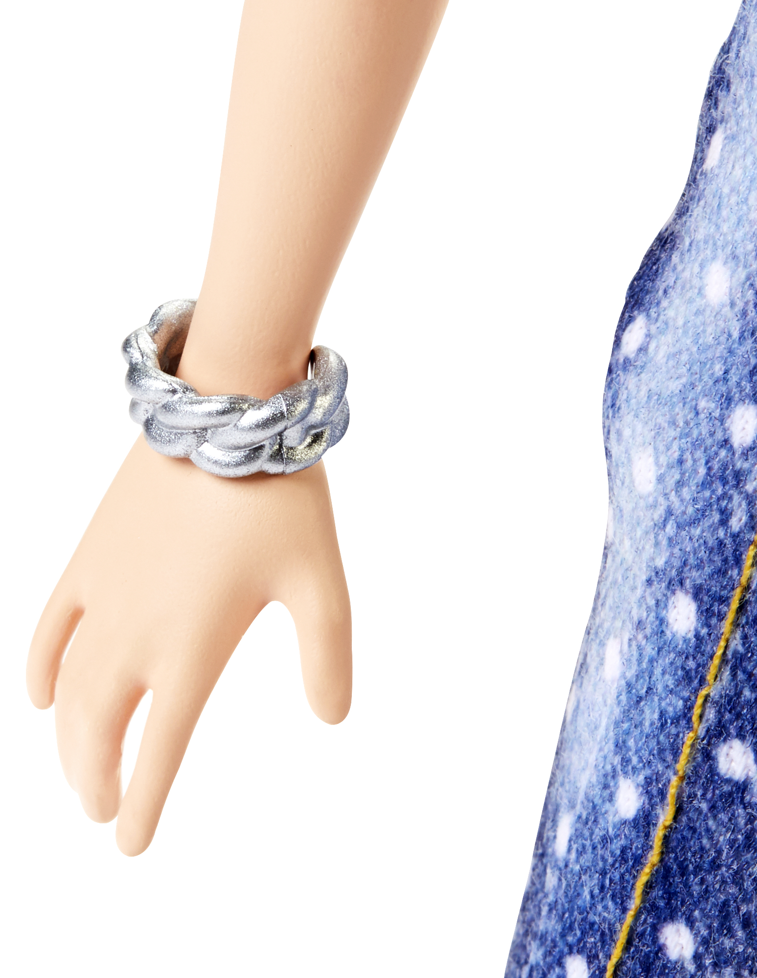 Der Arm einer Barbie-Puppe mit einem silbernen geflochtenen Armband am Handgelenk, Jeanskleid sichtbar.