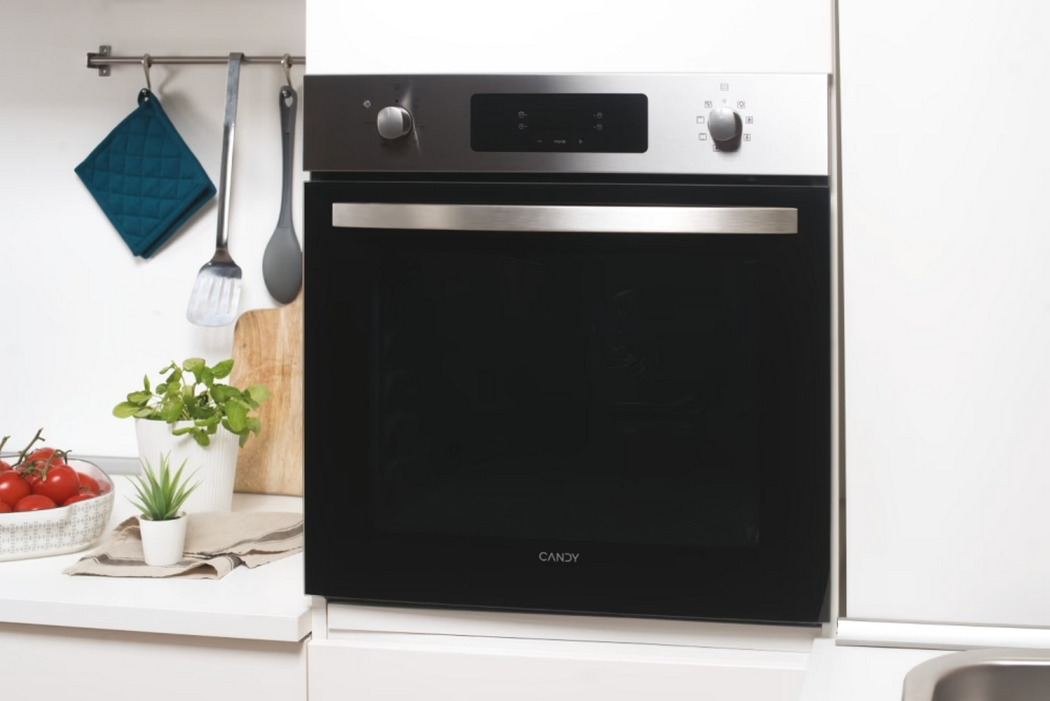 Forno con porta nera. Il piano di lavoro ha utensili, piante e alimenti.