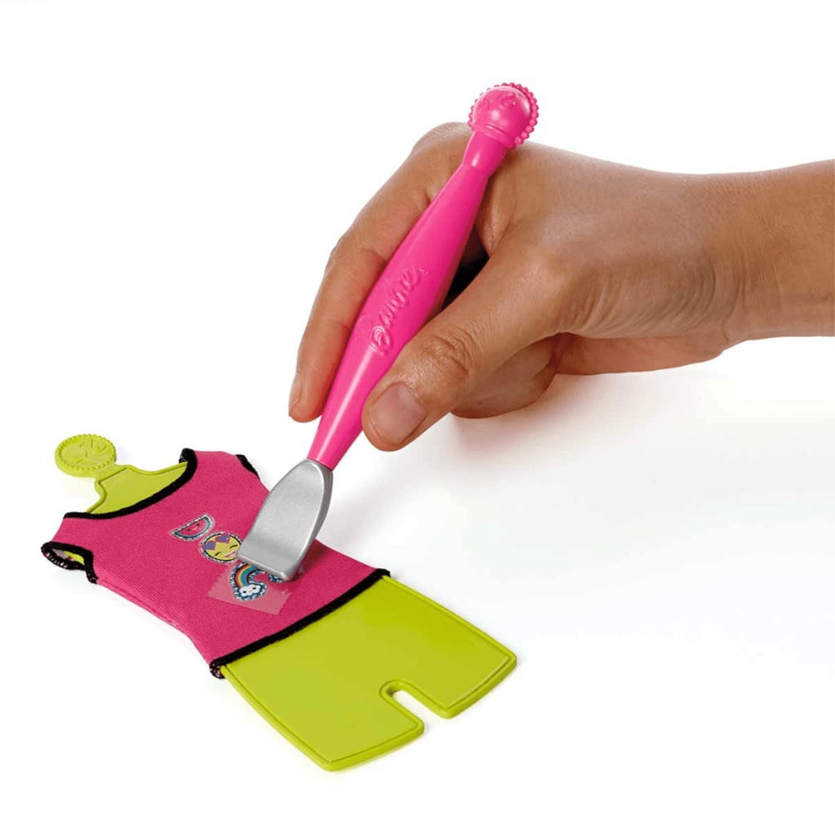 Eine Hand, die ein rosa Werkzeug verwendet, um einen Aufkleber auf die Kleidung einer Puppe anzubringen.