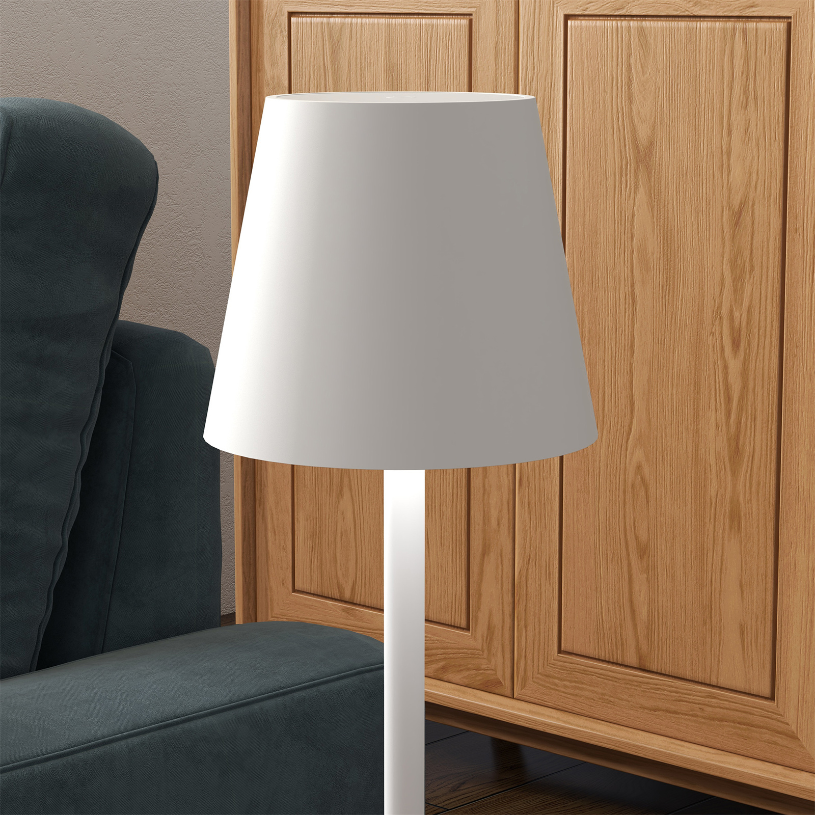 Weiße Lampe mit weißem Schirm neben türkisfarbenem Sessel und Holzschrank.