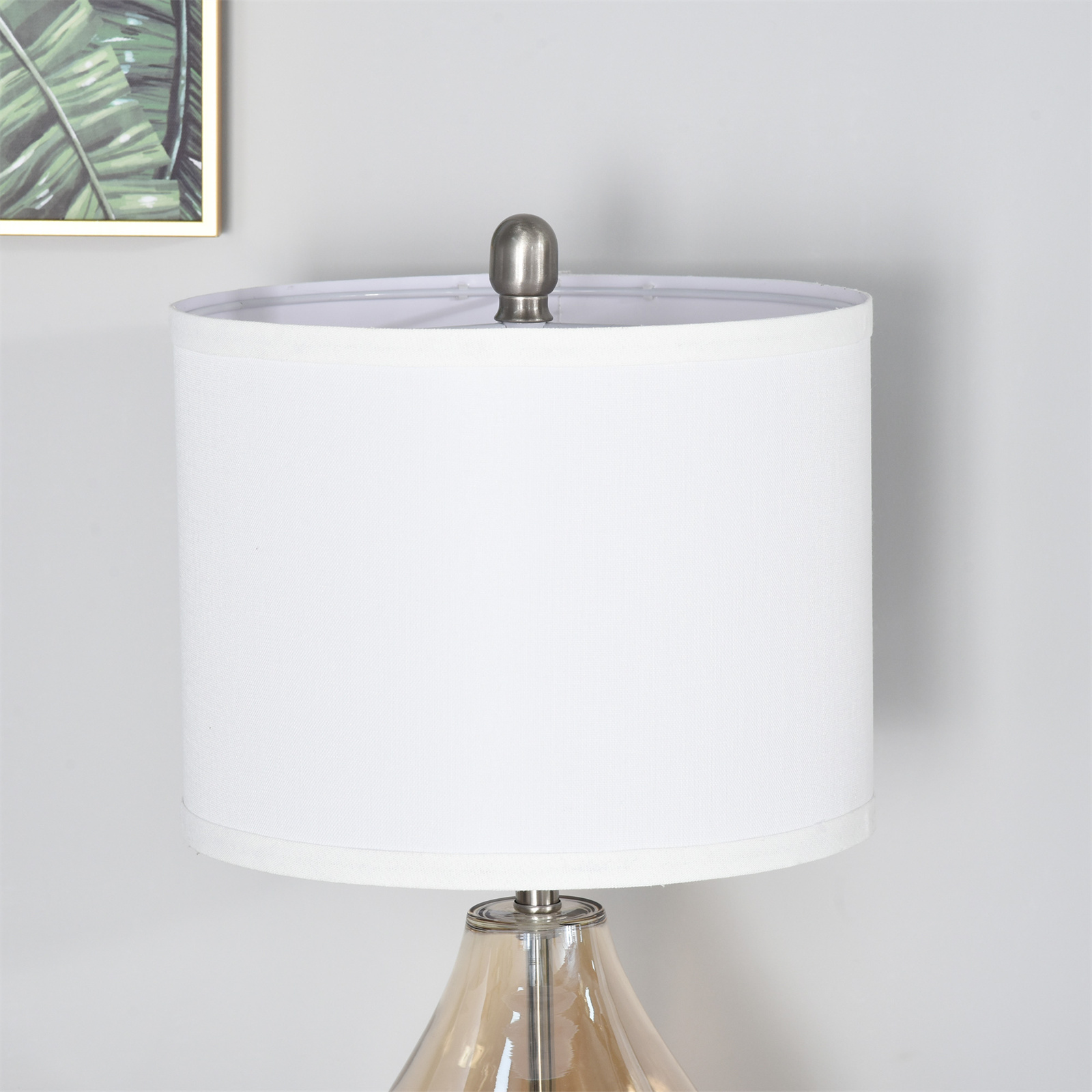 Nahaufnahme einer weißen Lampe mit weißem Schirm, silberner Basis, hellgraue Wand.